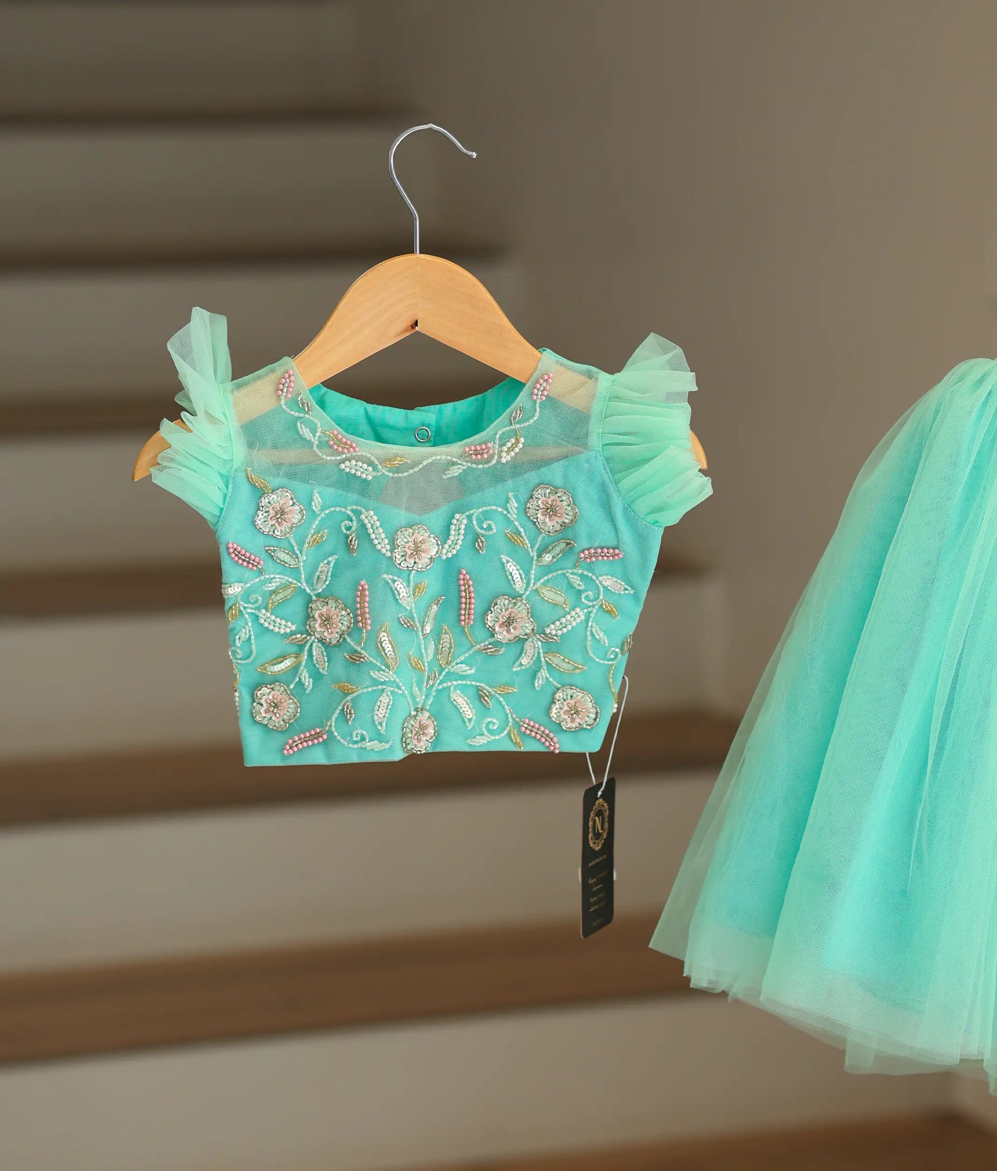 Close-up of the ocean green crop top showing the detailed flower embroidery and pretty ruffled sleeves