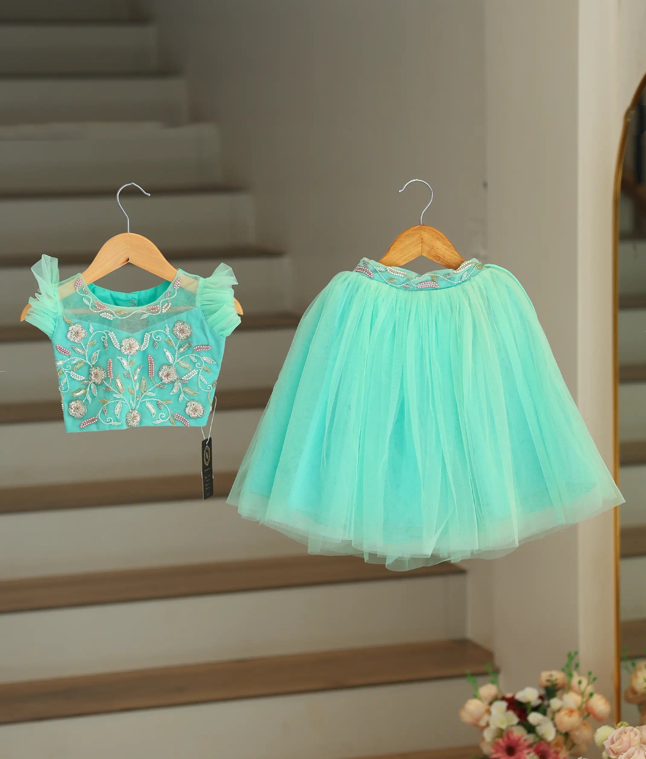 Front view of a baby girl wearing an ocean green handworked crop top and a long, fluffy tulle skirt