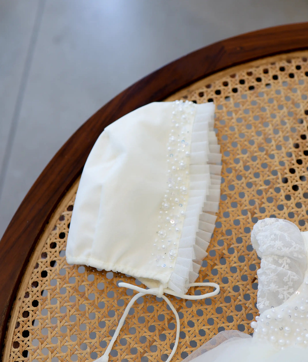 Close-up view of off-white baby girl baptism bonnet featuring pleated tulle trim and delicate pearl beadwork detailing.