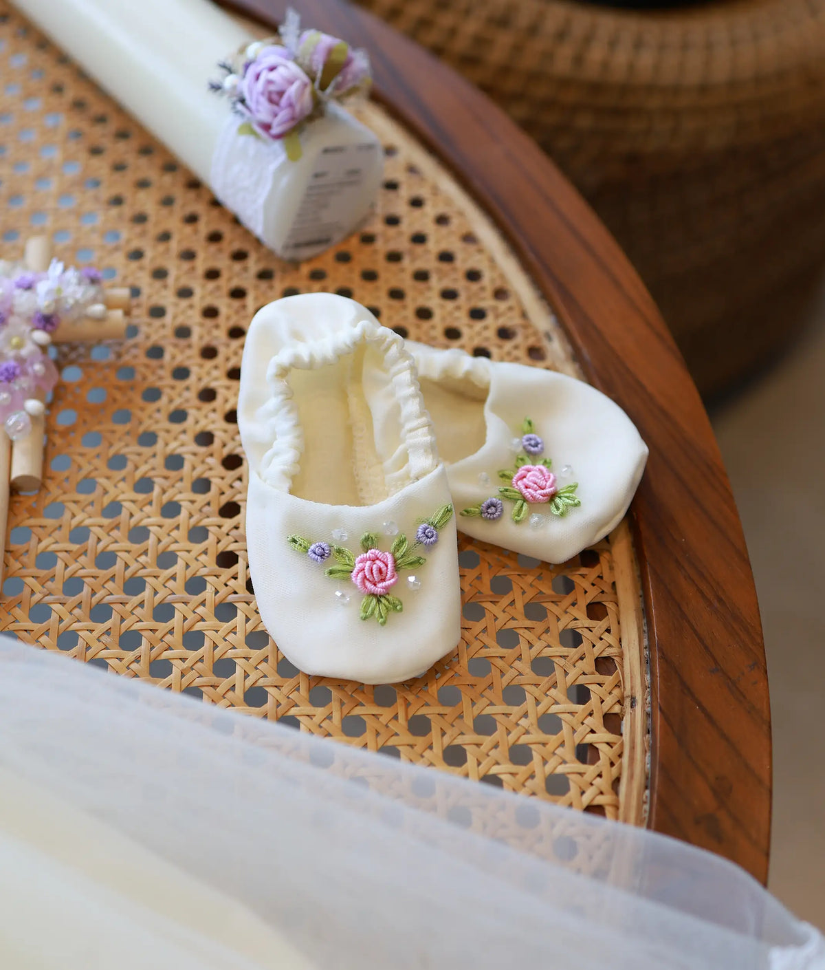 Close-up of off-white soft baby booties decorated with hand-embroidered floral roses and pearls for baptism set.