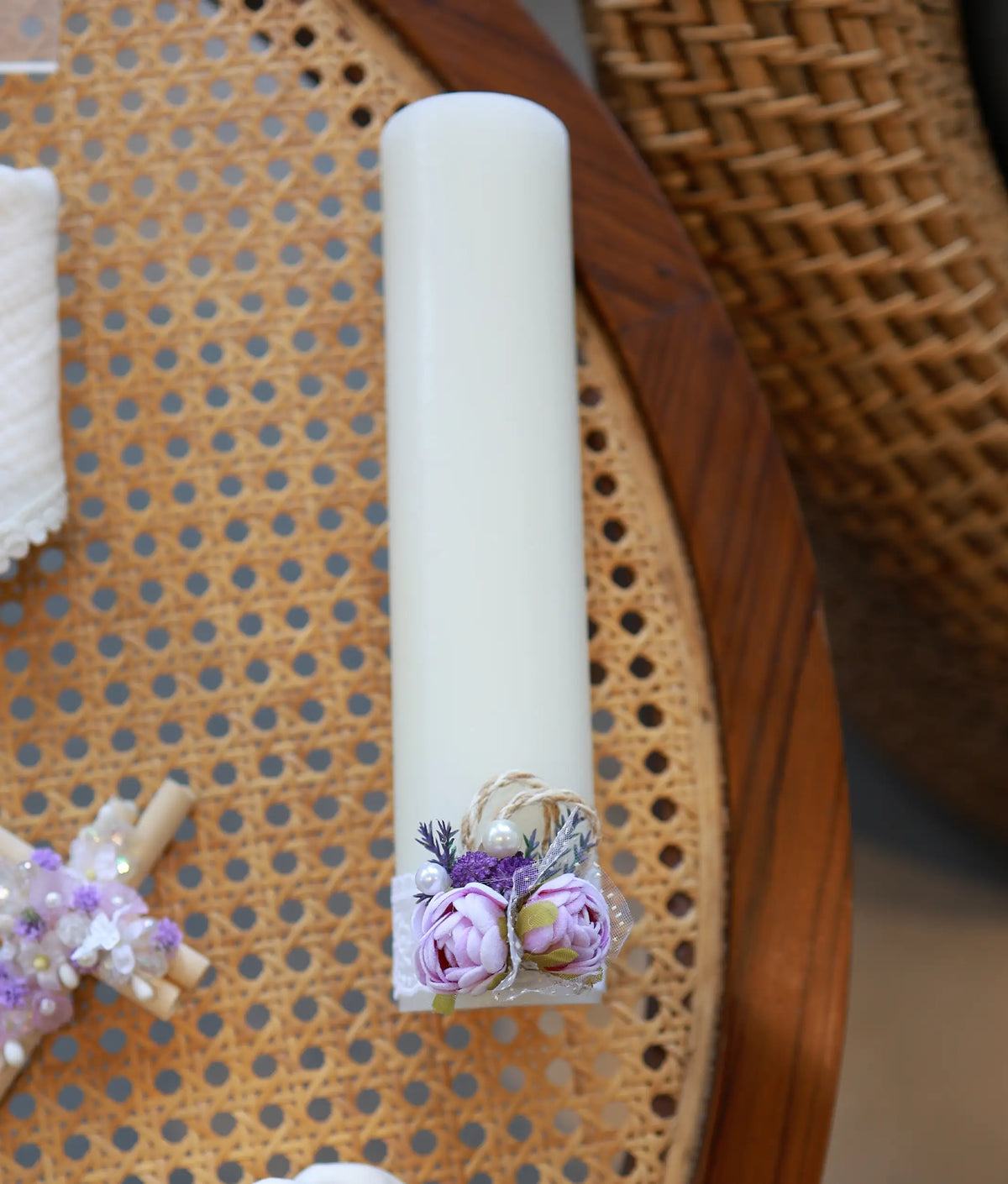 Off-white baptism candle decorated with lace trim, pearls, and purple flower embellishments.