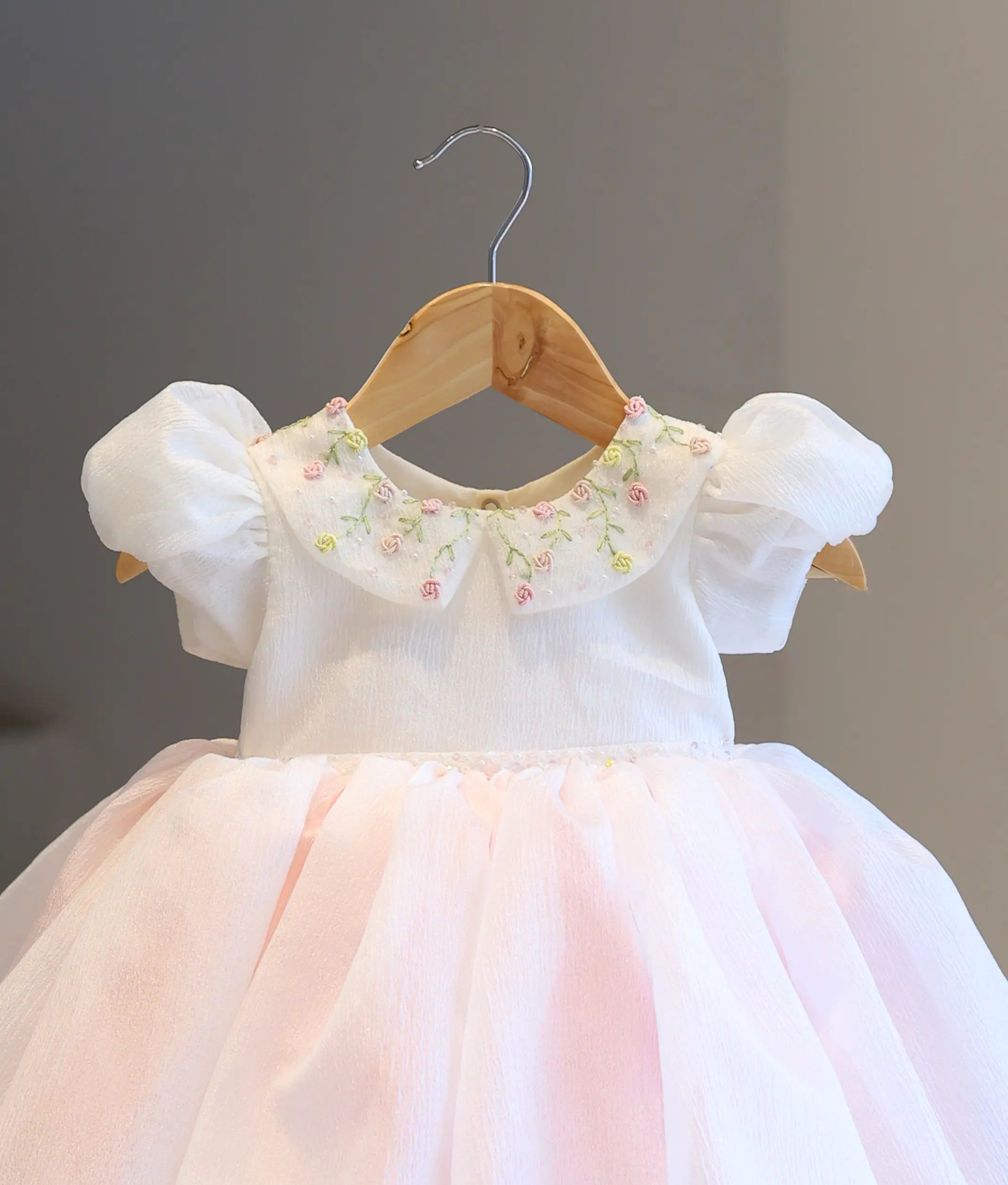 Close-up detailing of the off-white dress bodice, highlighting the hand-embroidered blush pink floral motifs and the textured crush organza puff sleeve.