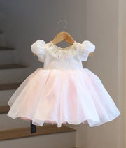 Full-length front view of the off-white and blush pink crush organza baby frock on a hanger, showcasing the floral embroidered top and the flared blush pink bottom.