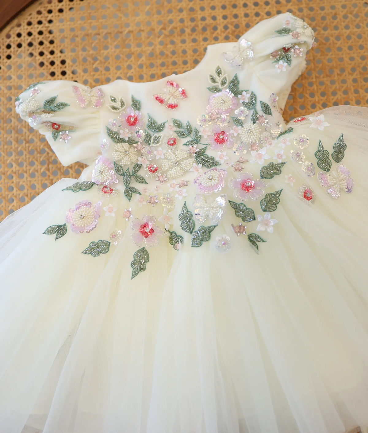 Close-up view of off-white christening frock showing handworked floral embroidery with pearls, sequins, and butterflies.