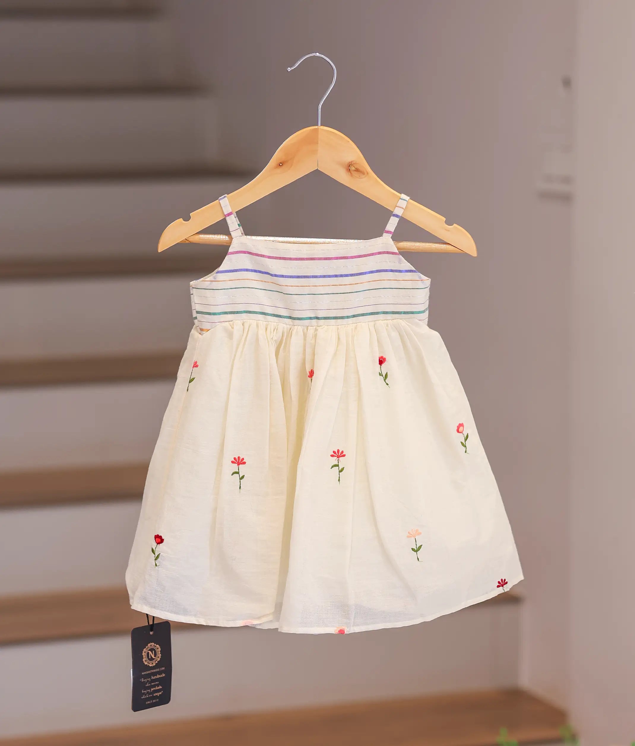 Front view of an off-white cotton frock for girls featuring small embroidered flowers and thin straps.