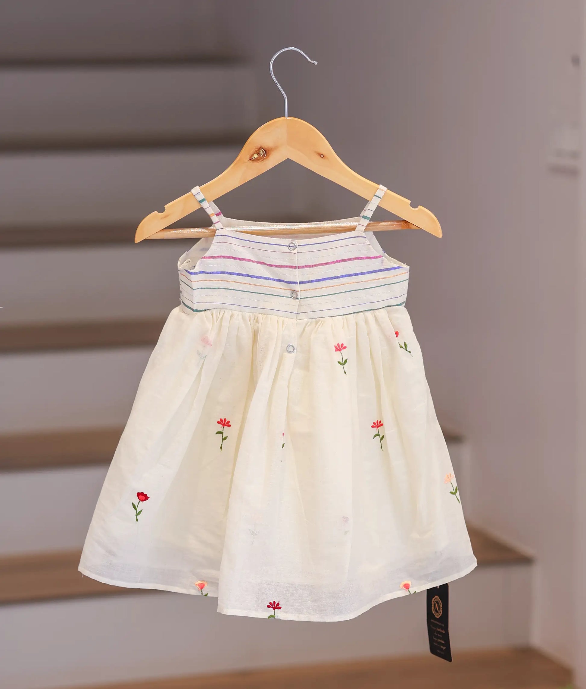 Back view of the off-white cotton frock highlighting the striped straps and press button closure.