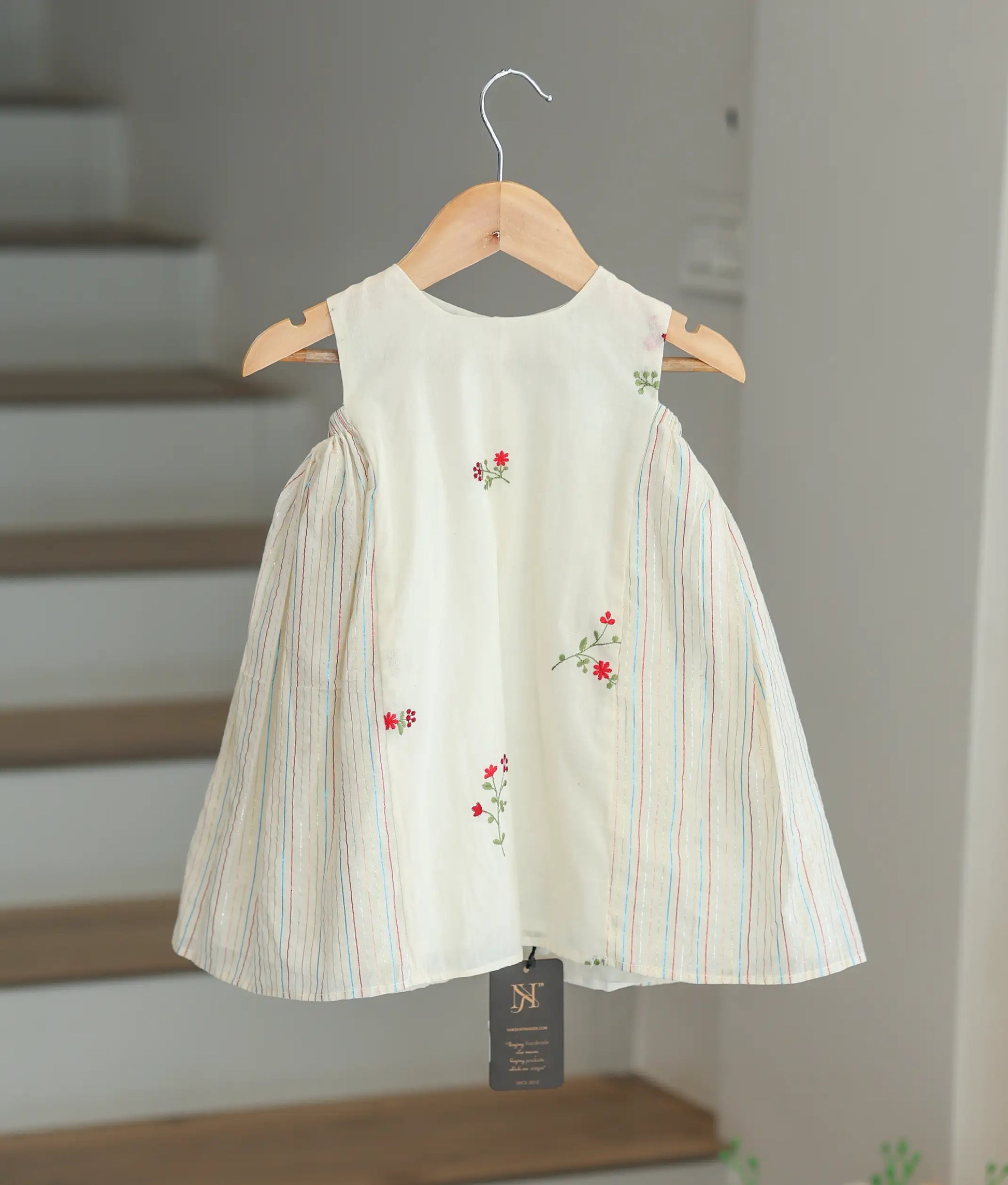 Front view of a sleeveless off-white cotton casual frock with a floral print and striped side detailing.