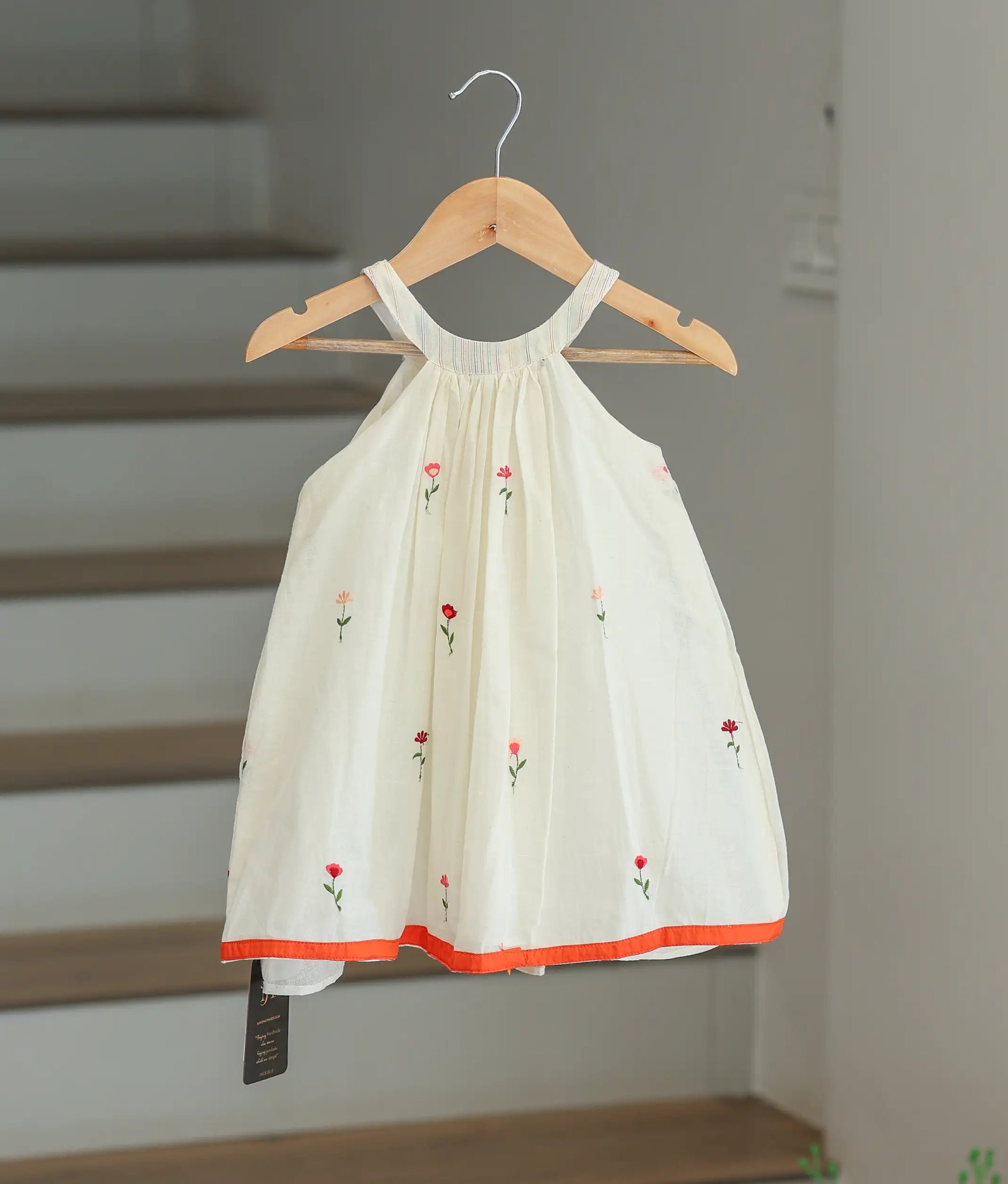 Front view of an off-white cotton printed frock for girls with a floral pattern and orange hem border.