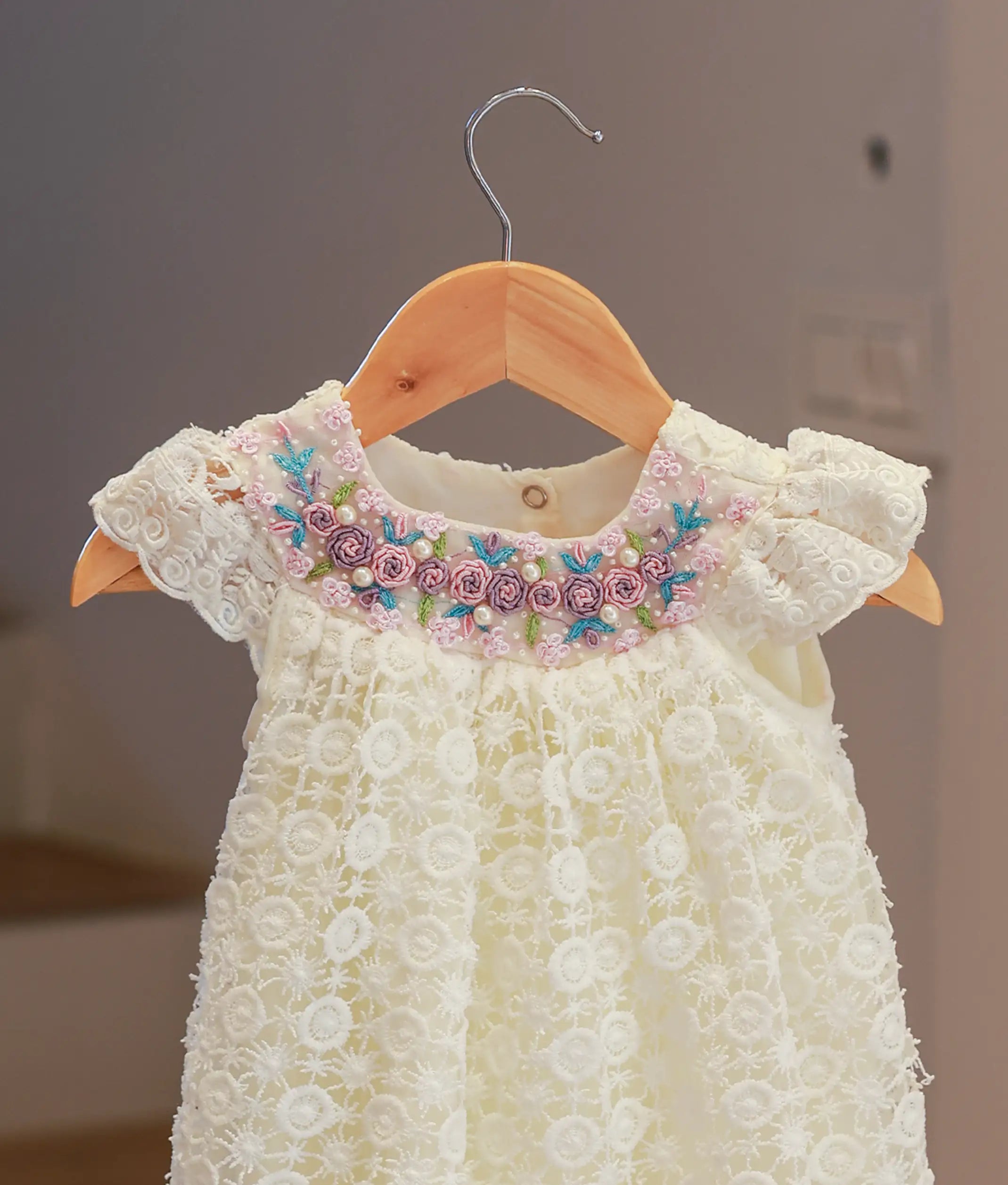 Close-up detail of the off-white baptism frock highlighting the artisanal hand-worked crochet patterns and textured floral motifs.