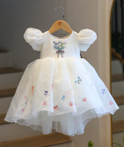 Full front view of the off-white high-low crush organza kids frock on a hanger, highlighting the elegant high-low hemline, butterfly prints, and hand-embroidered flower bouquet.