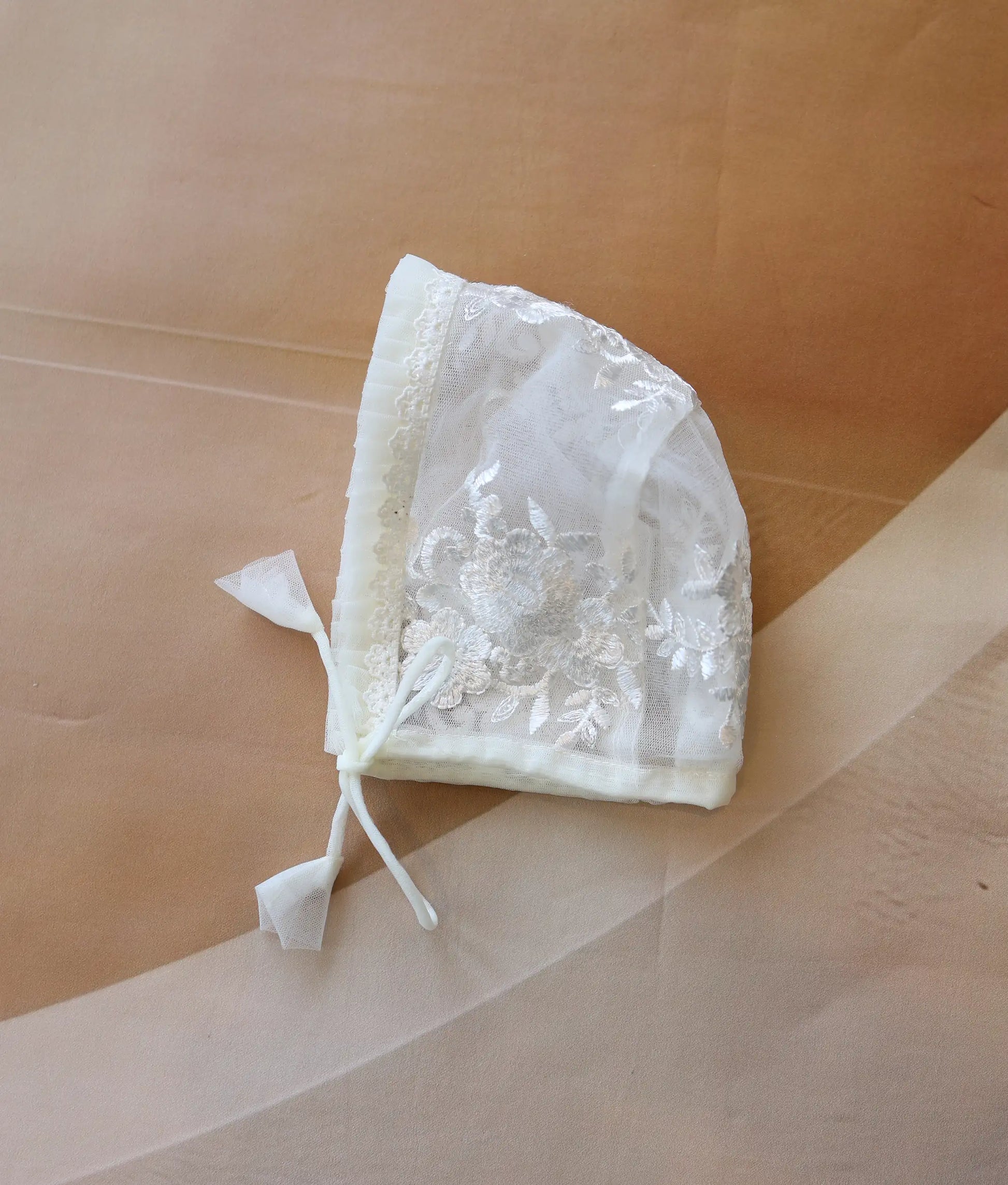 Front view of an off-white baby christening bonnet made from floral work material.