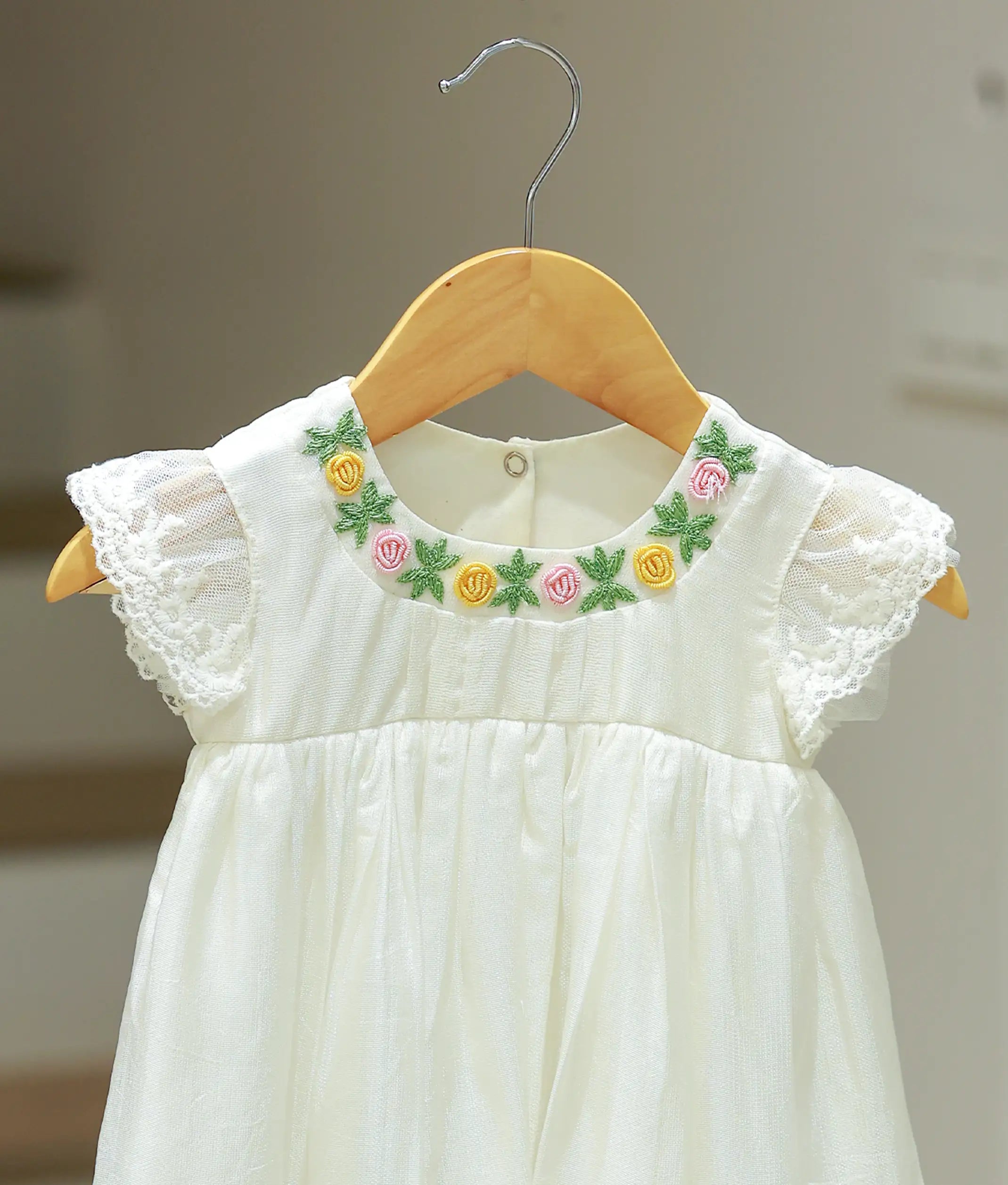 Close-up view of the off-white baptism frock highlighting the intricate floral embroidery patterns and fine threadwork.