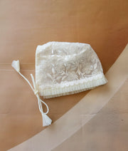 Front view of an off-white baby christening bonnet made from floral work material.