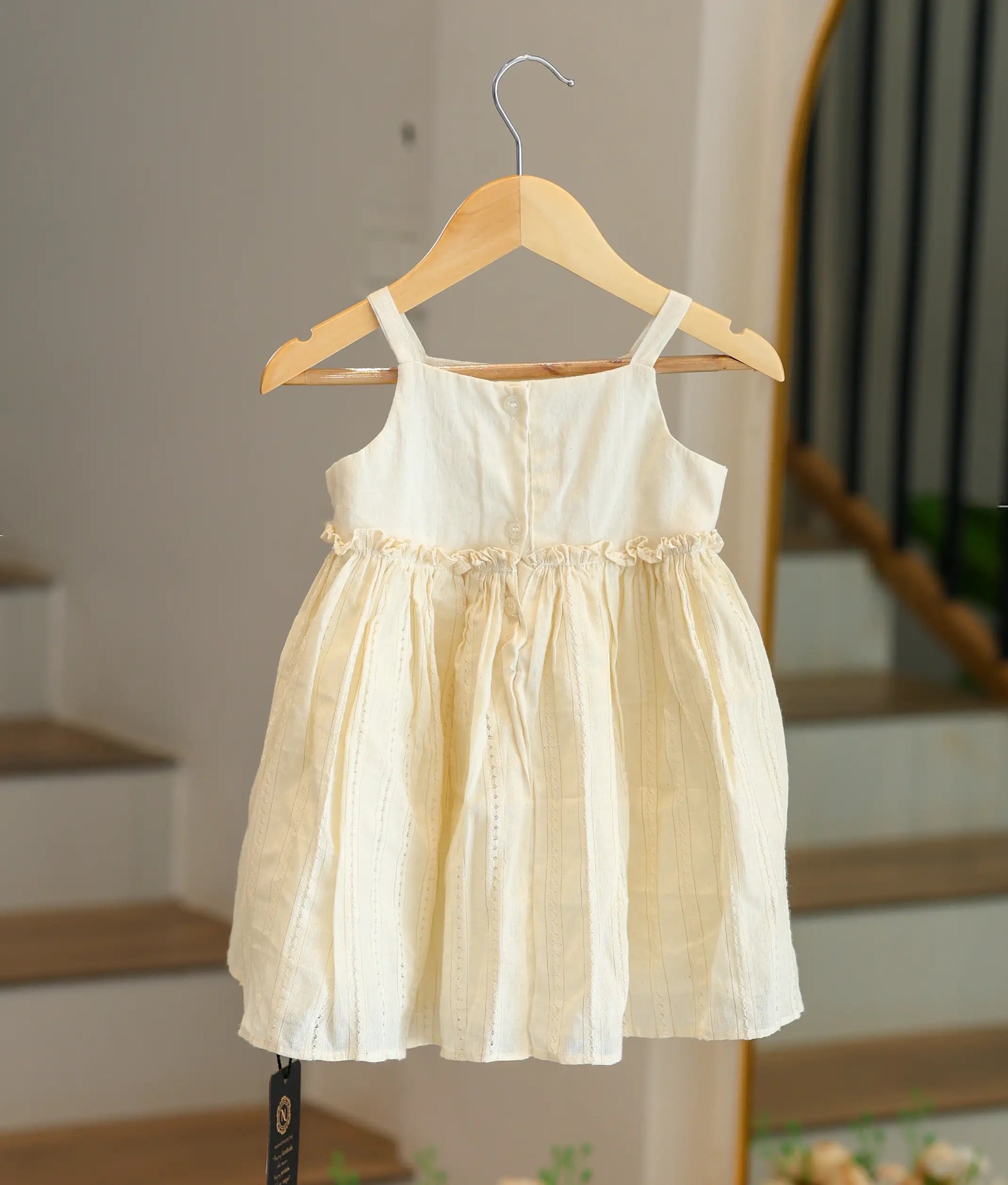Back view of the off-white Kasavu cotton frock showing the button closure and vertical gold-thread stripes