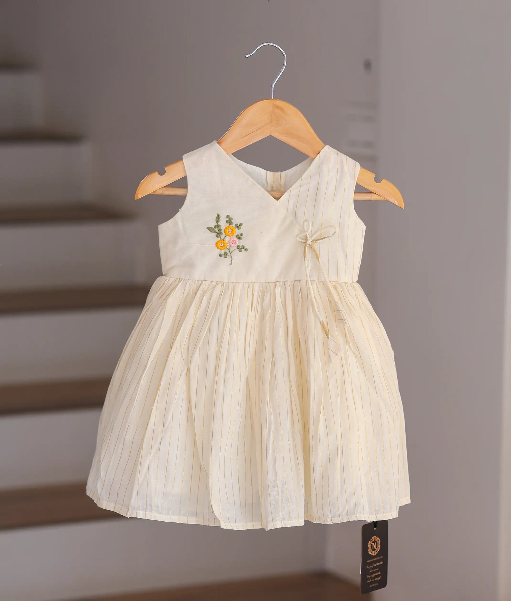 Front view of an off-white cotton frock for baby girls featuring colorful hand-embroidered flowers