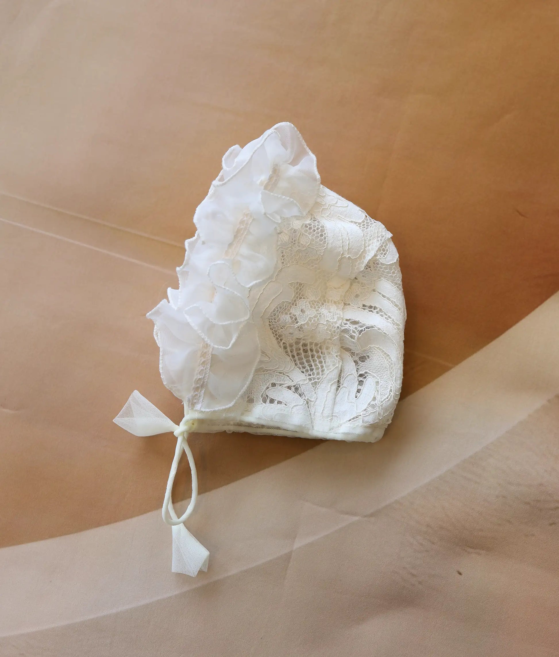 Front view of a baby's off-white baptism cap with ruffled lace edges.