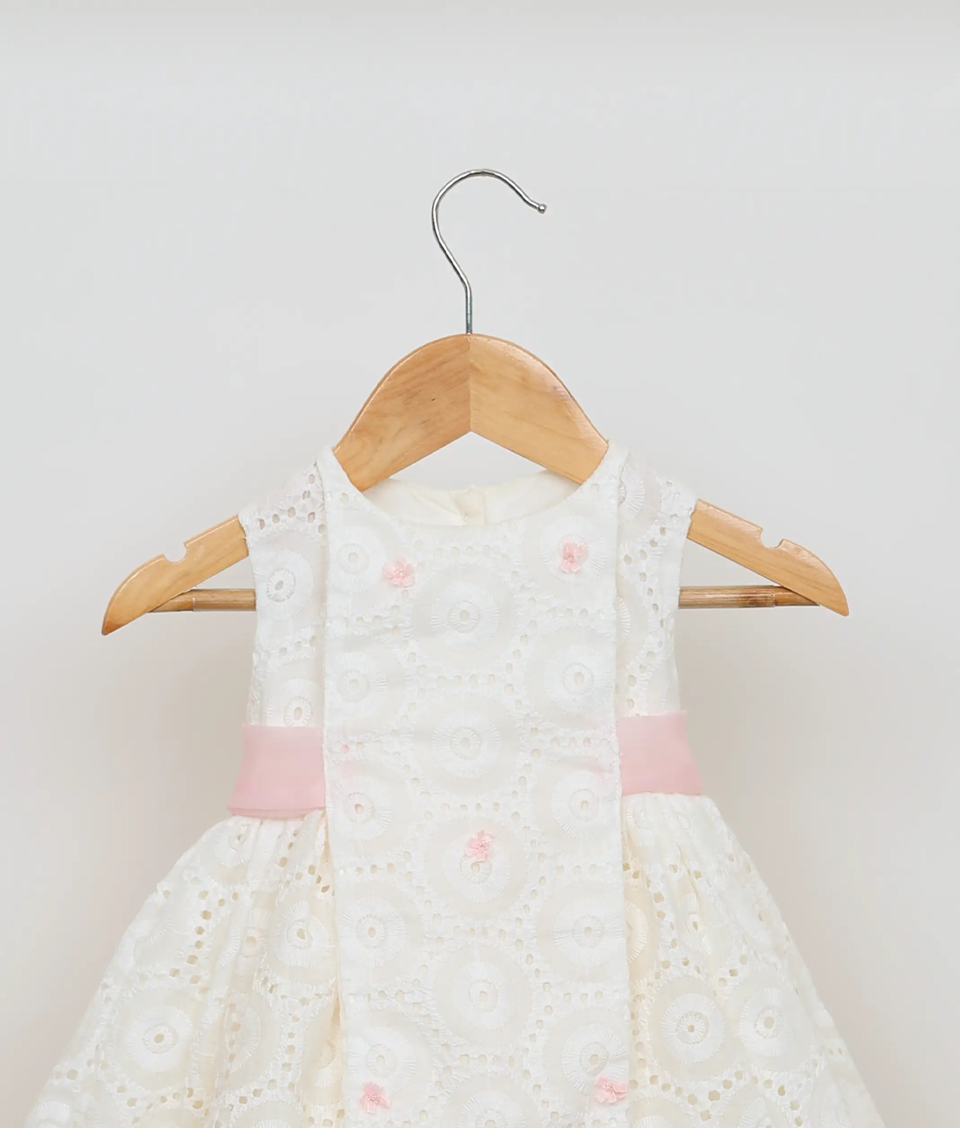 Close view of an hacoba embroidery yoke and pink ribbon central sash on the off-white baby girl frock.