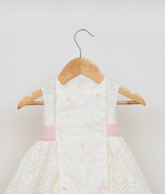 Close view of an hacoba embroidery yoke and pink ribbon central sash on the off-white baby girl frock.