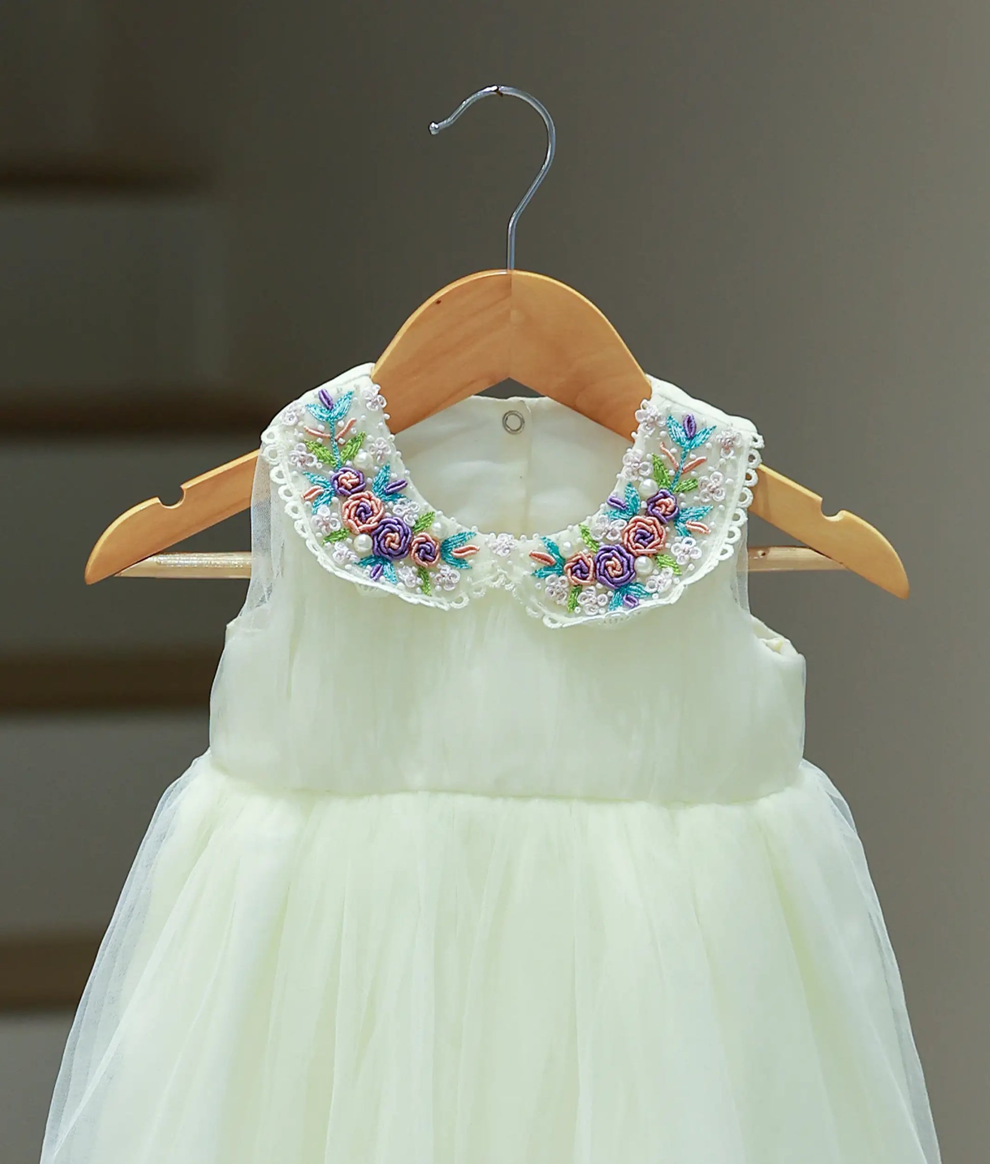 Close-up of the off-white baptism frock showing the Peter Pan collar with purple and yellow floral embroidery and the matching floral crown.