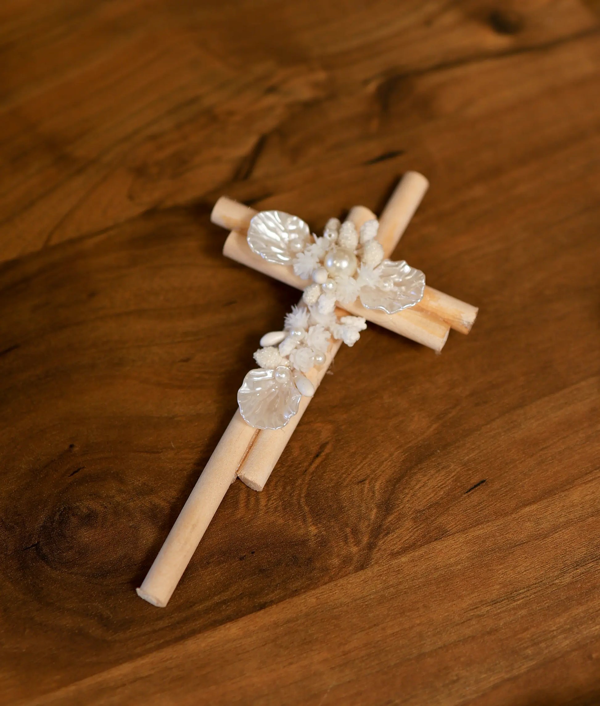 Wooden baptism cross decorated with delicate white shell flowers, pearl beads, and fabric floral embellishments.