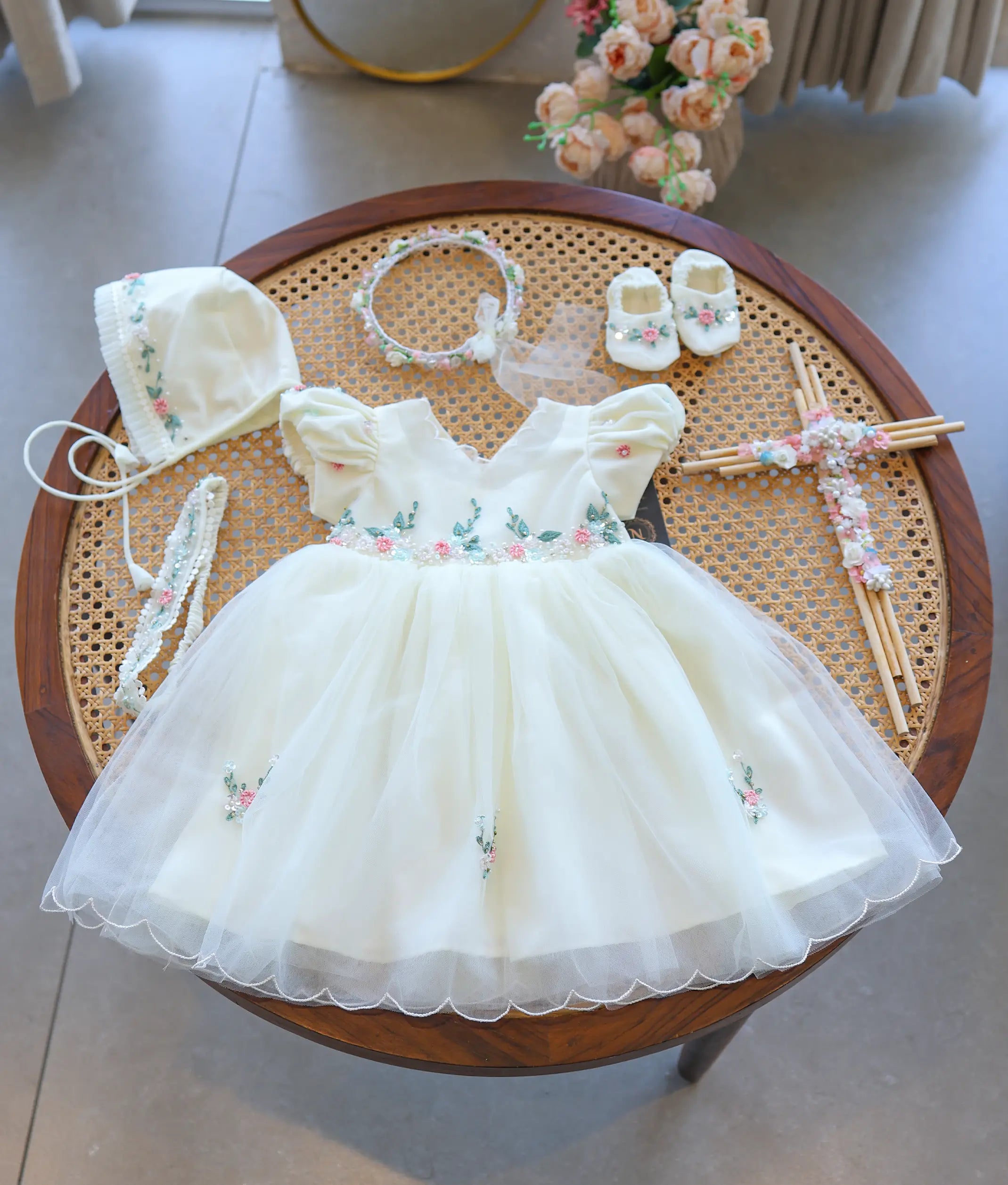 Off-white baptism set for baby girl featuring a tulle net dress with embroidered waistline displayed with matching bonnet, headband, booties, and cross accessory.
