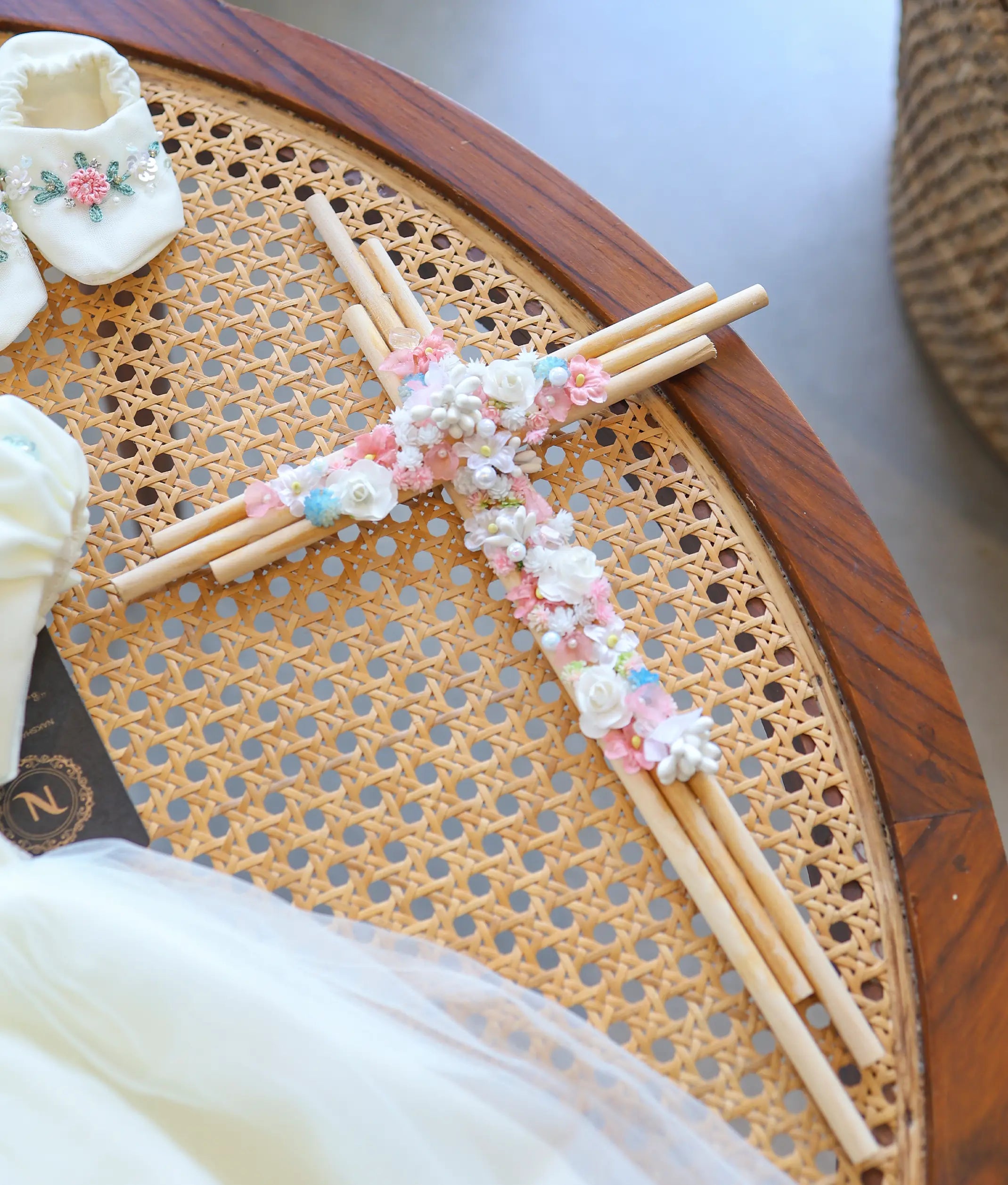 Close-up of baptism candle cross accessory decorated with handcrafted white and pink flowers, pearls, and greenery.