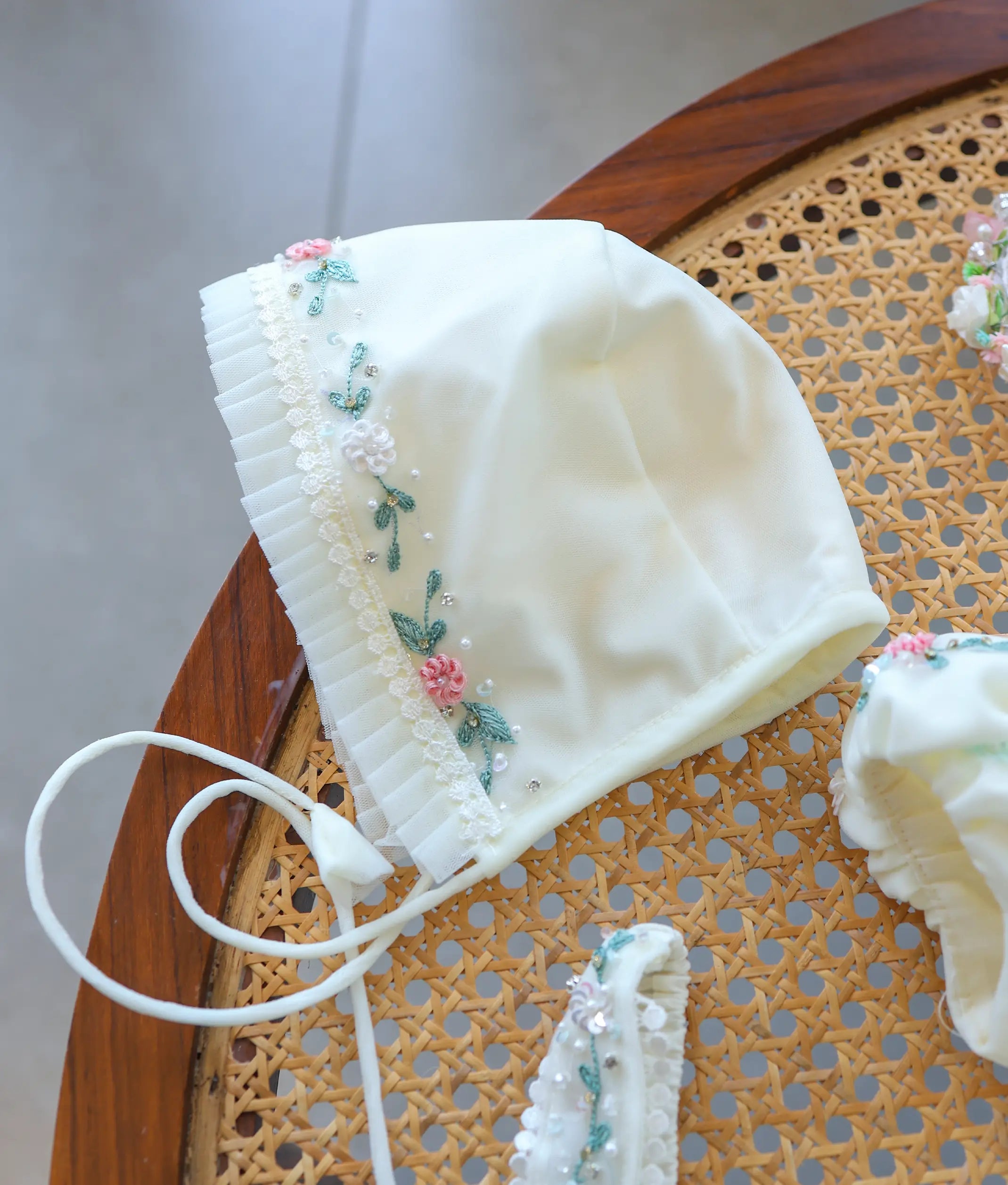 Off-white baby girl baptism bonnet with ruffled net trim and matching floral handwork embroidery.