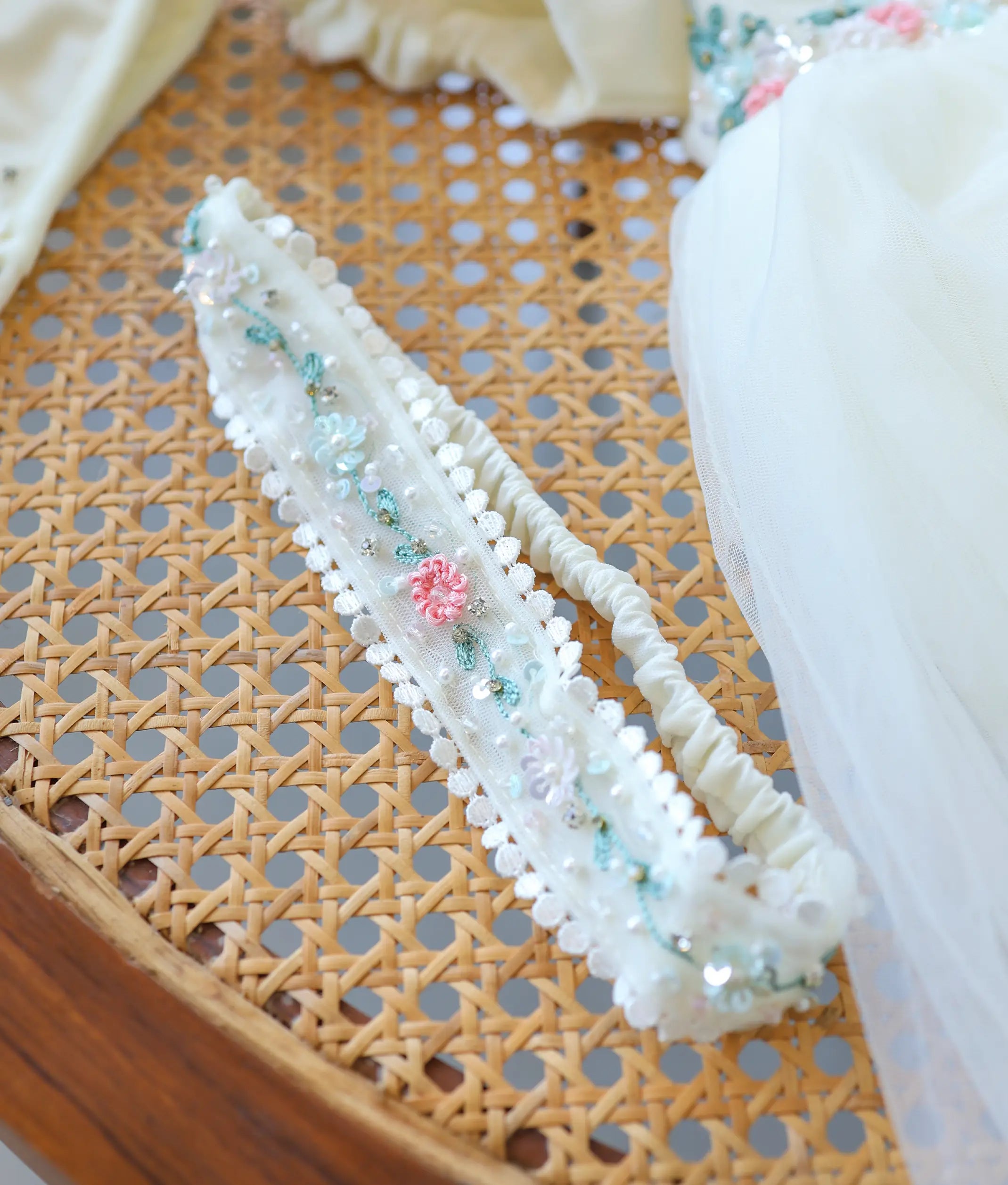 Close-up of elastic lace headband accessory adorned with pink embroidered flowers and beaded accents.