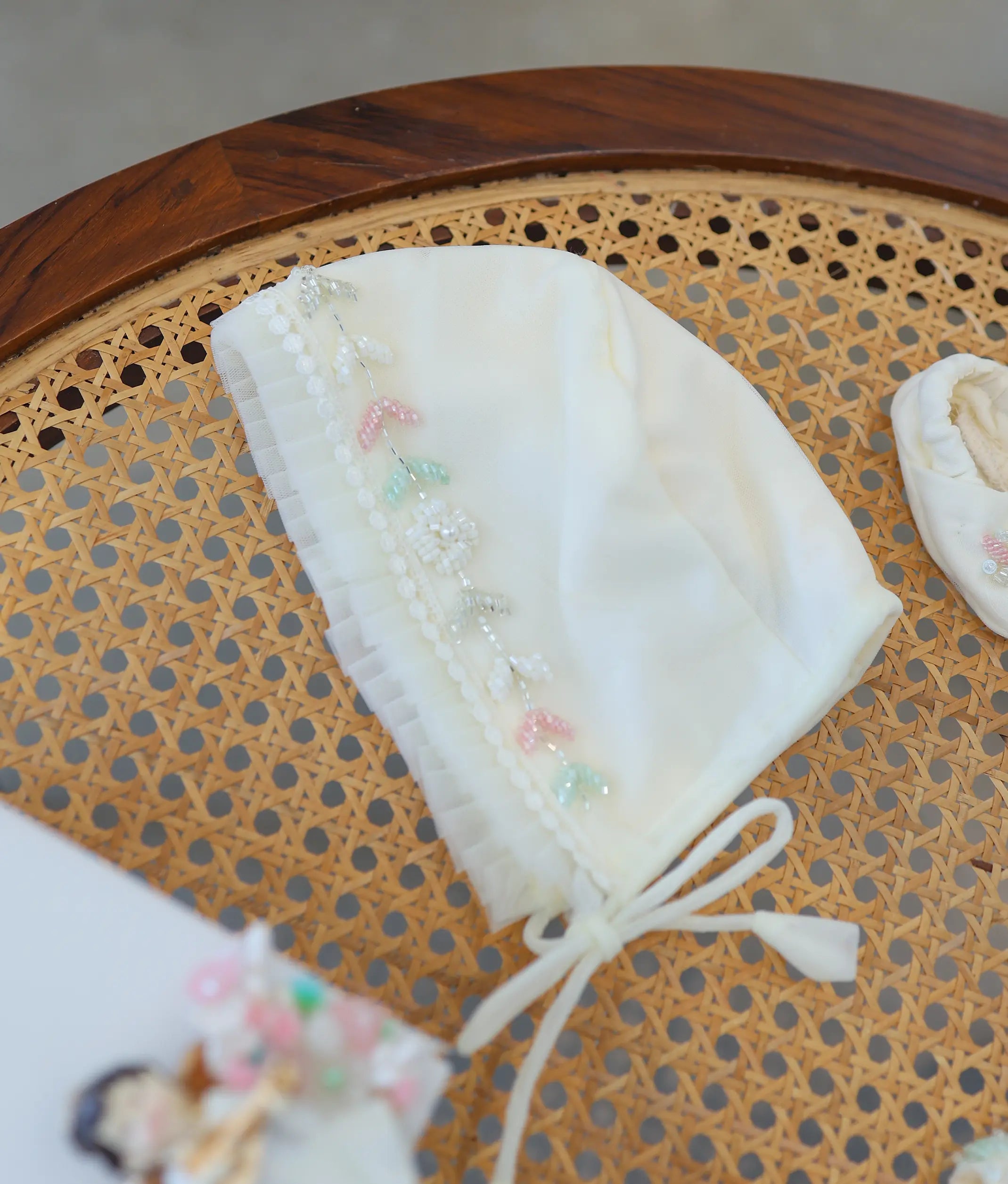 Off-white baby girl baptism bonnet with pleated net trim and pastel floral handwork embroidery with bead details.