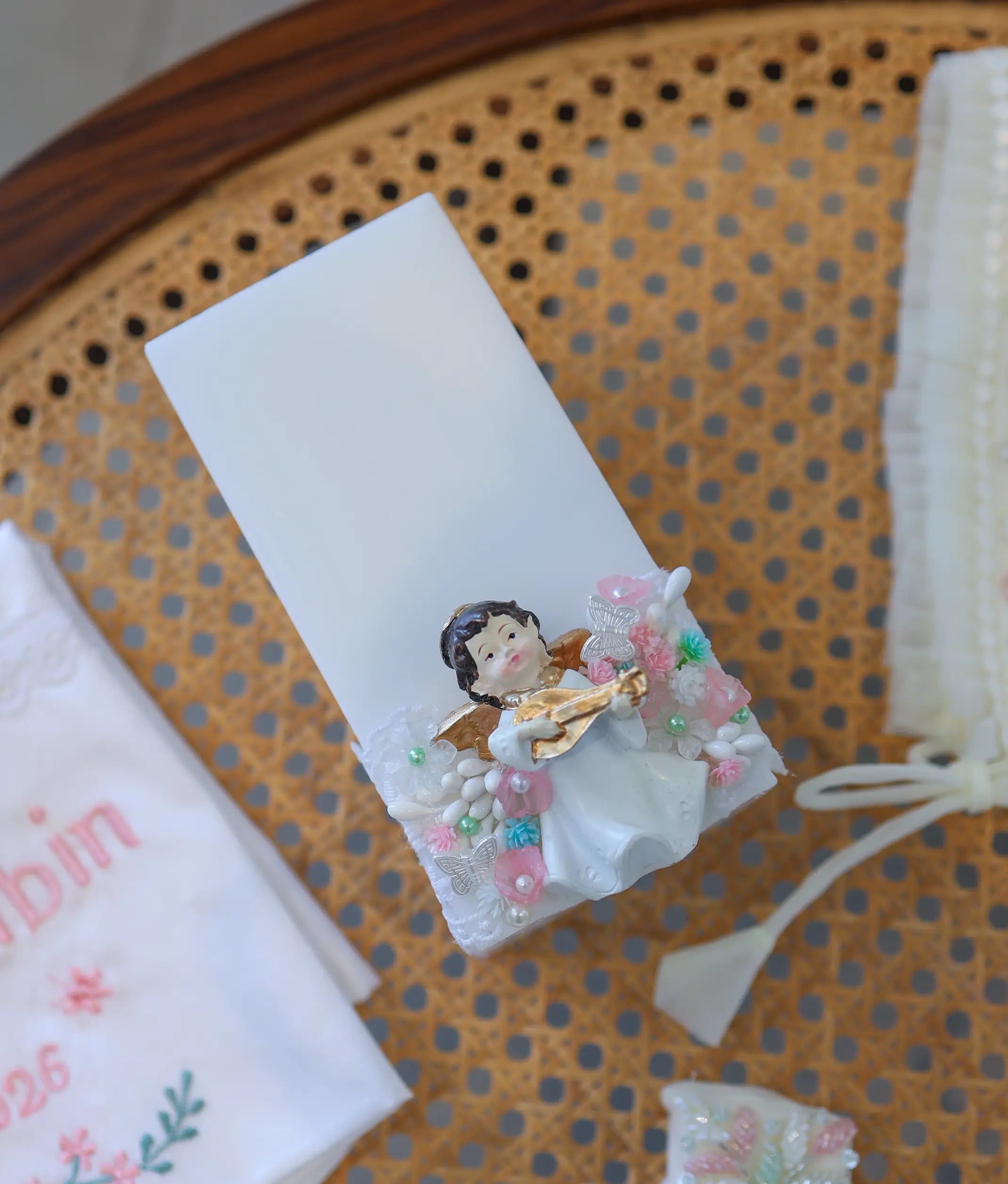 Square white baptism candle decorated with an angel figurine, lace wrap, and handcrafted floral accents.