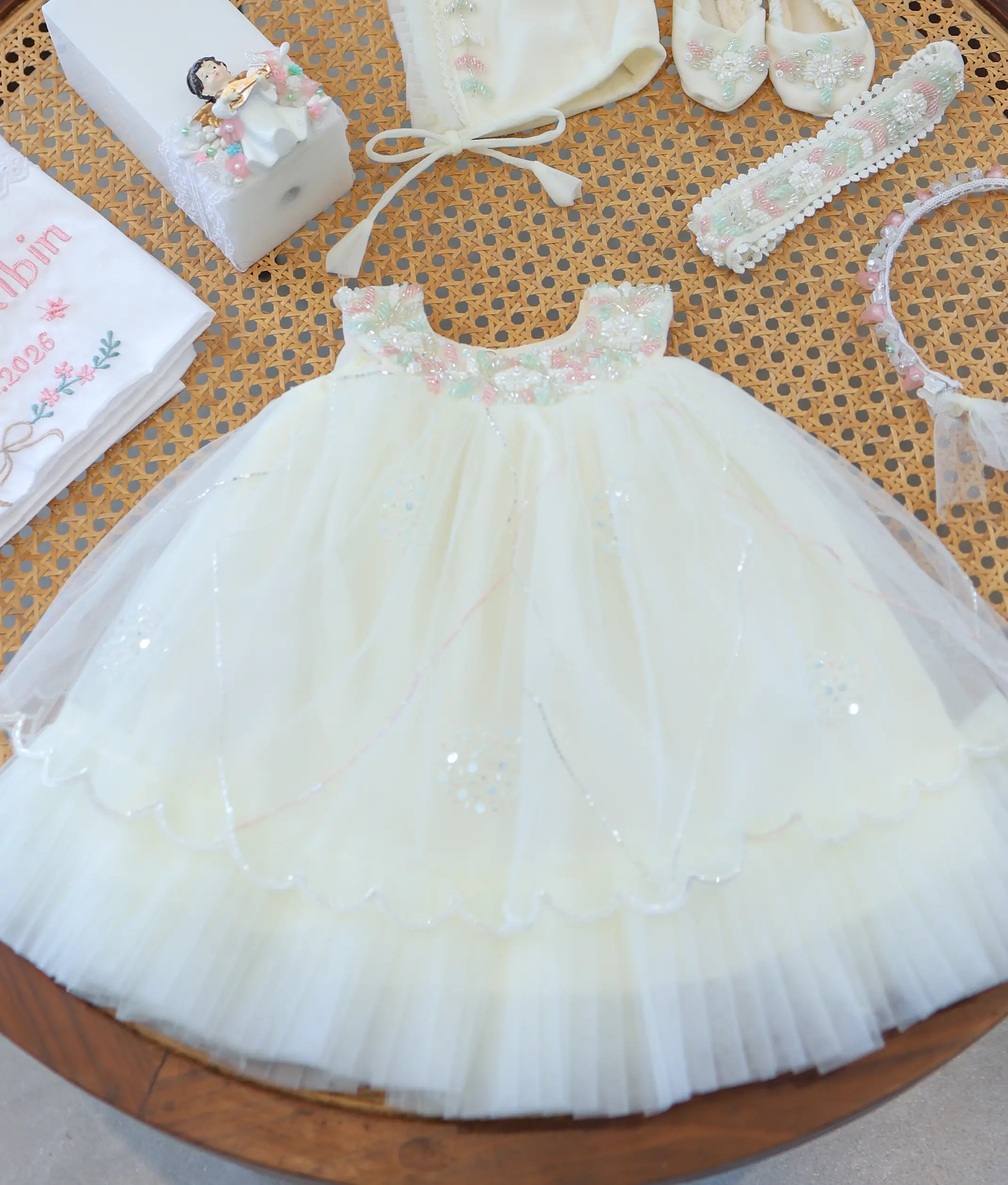 Off-white baby girl baptism dress with scalloped tulle net layers and pastel floral beadwork on the neckline.