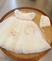Full off-white baby girl baptism set with pink and silver waist embroidery, matching bonnet cap, booties, and headband on a cane table.