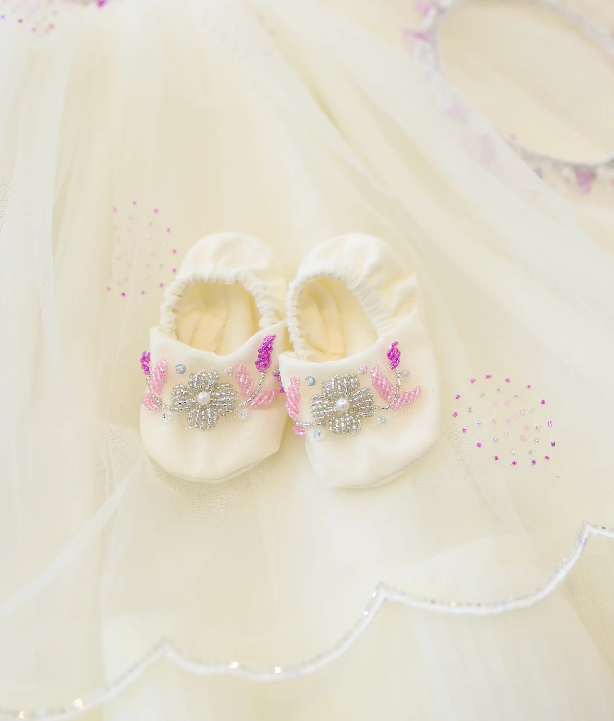 Off-white soft baptism booties for baby girl decorated with silver bead flowers and pink leaves.Off-white soft baptism booties for baby girl decorated with silver bead flowers and pink leaves.