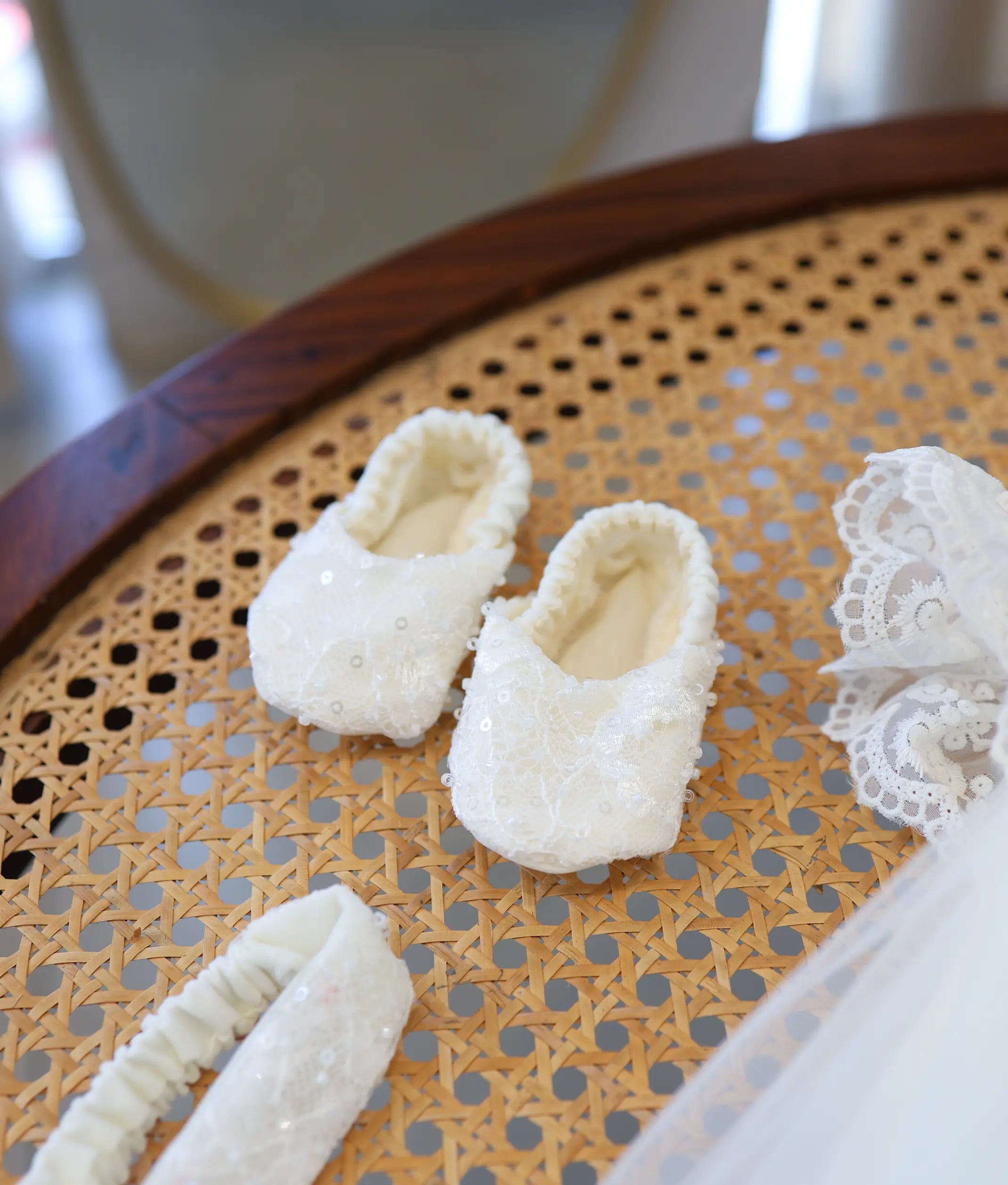 Pair of soft off-white baptism booties for baby girl decorated with sequin lace detailing.