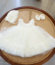 Complete off-white handwork baptism set for baby girl featuring pearl-embellished net frock, matching bonnet cap, and handworked booties on a woven cane table