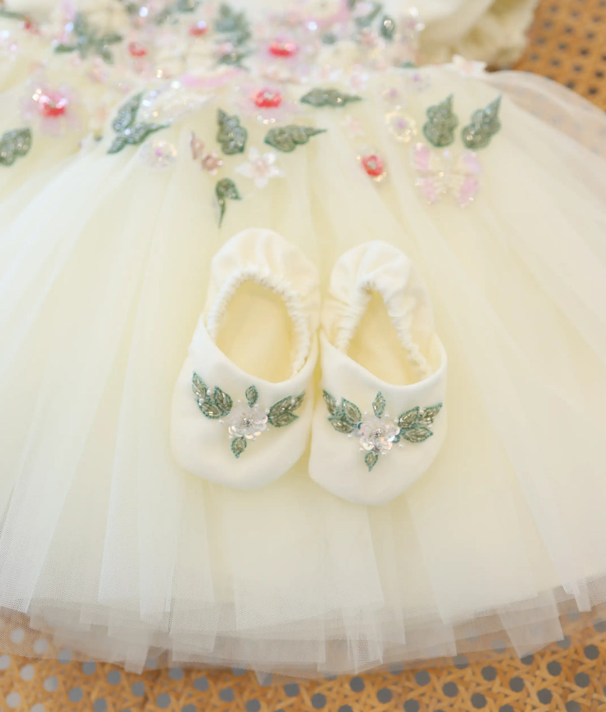 Close-up view of off-white handworked baby booties with floral embroidery for christening dress set.
