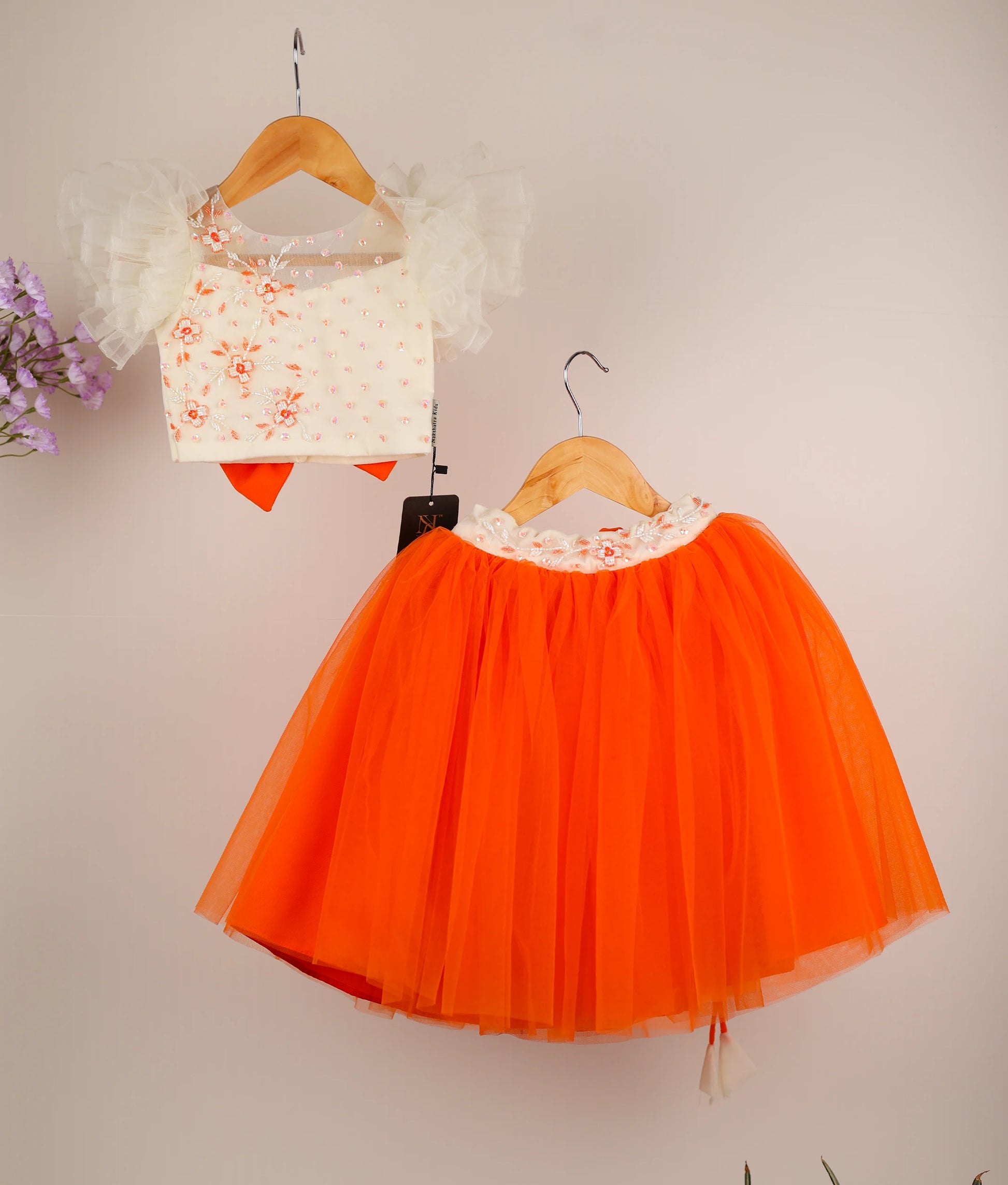 Front view of a girls' off-white handworked crop top with butterfly sleeves and a full-length orange tulle skirt