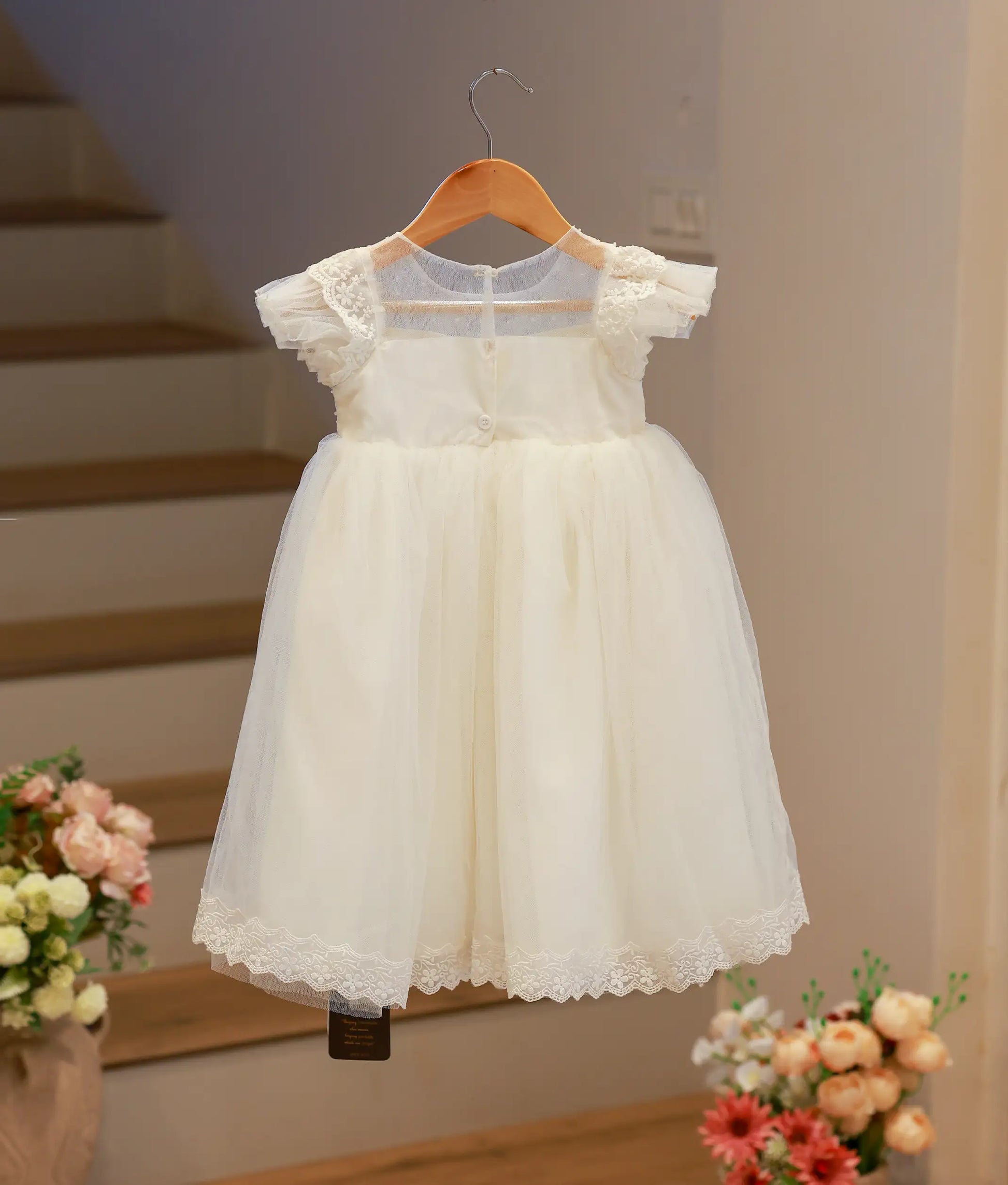 Back view of the off-white handworked baptism frock highlighting the elegant back profile and sheer tulle sleeves.