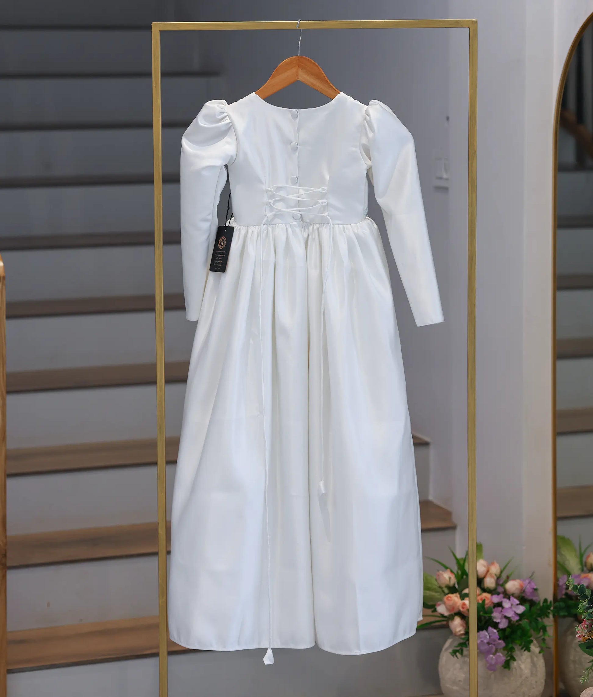 Back view of the off-white satin communion dress on a display stand, highlighting the vertical buttons and the adjustable corset lace-up tie system.