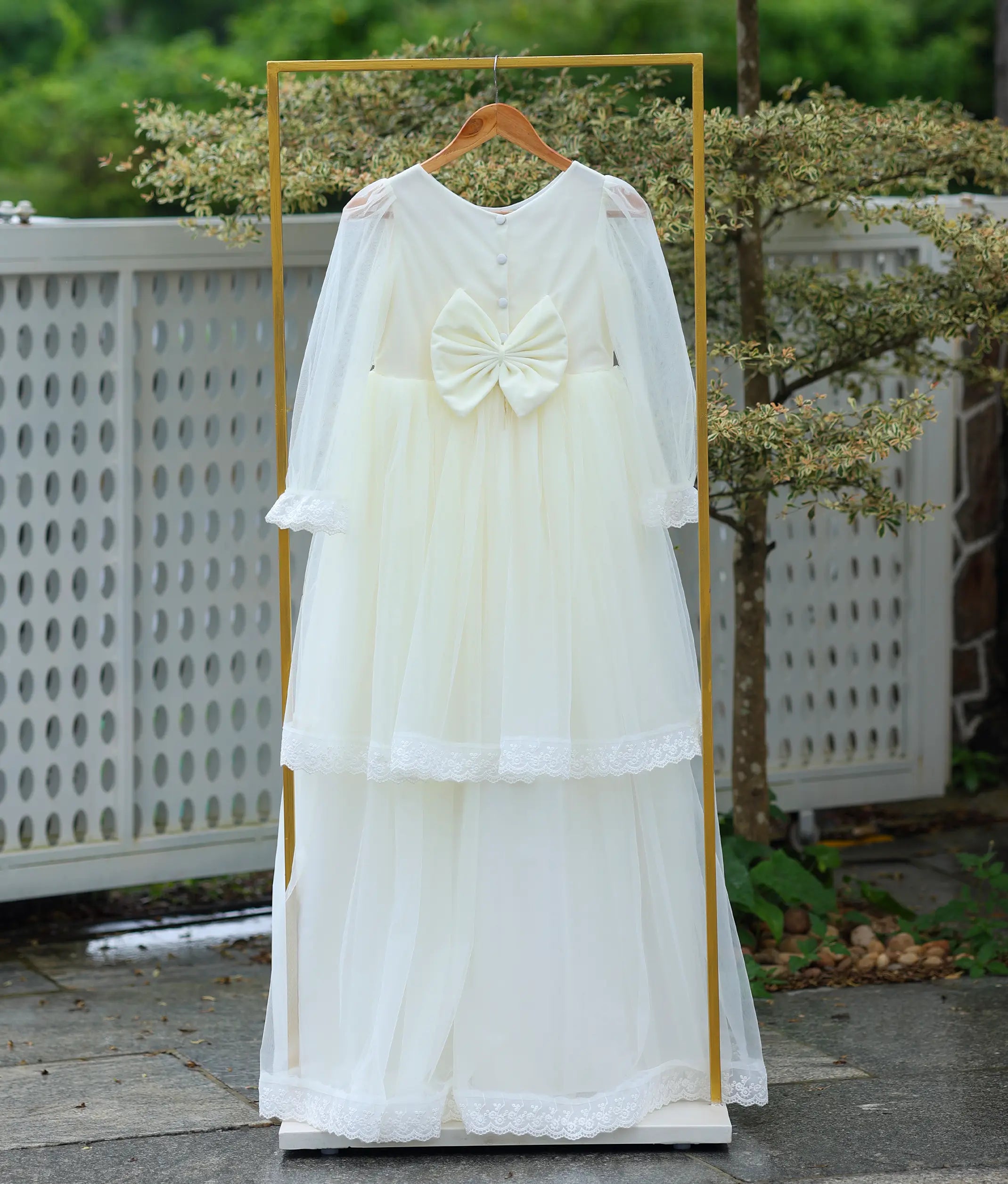 Back view of the off-white communion dress showing the vertical button closure and a large structured waist bow.