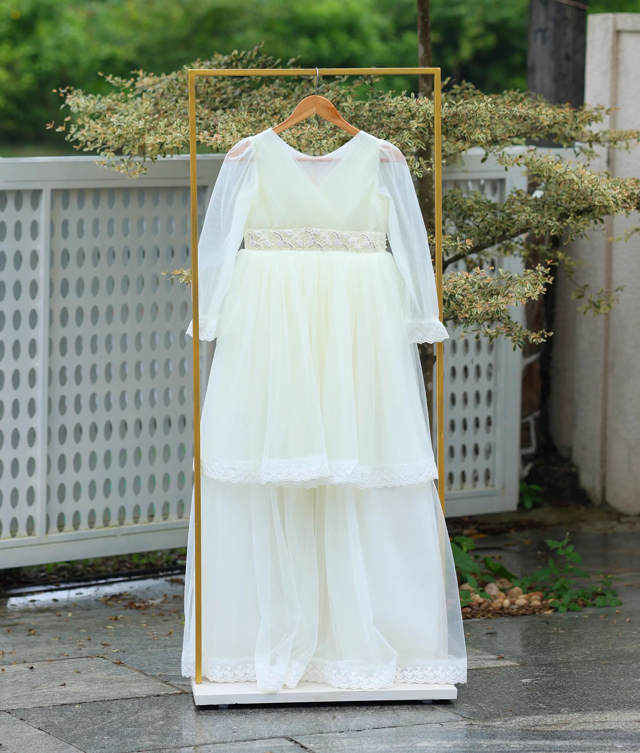 Full front view of the tiered off-white tulle Holy Communion gown hanging