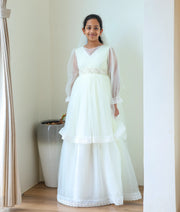 A girl smiling while wearing the Nakshatra Kids elegant off-white Holy Communion gown, complete with a matching sheer white net head veil.