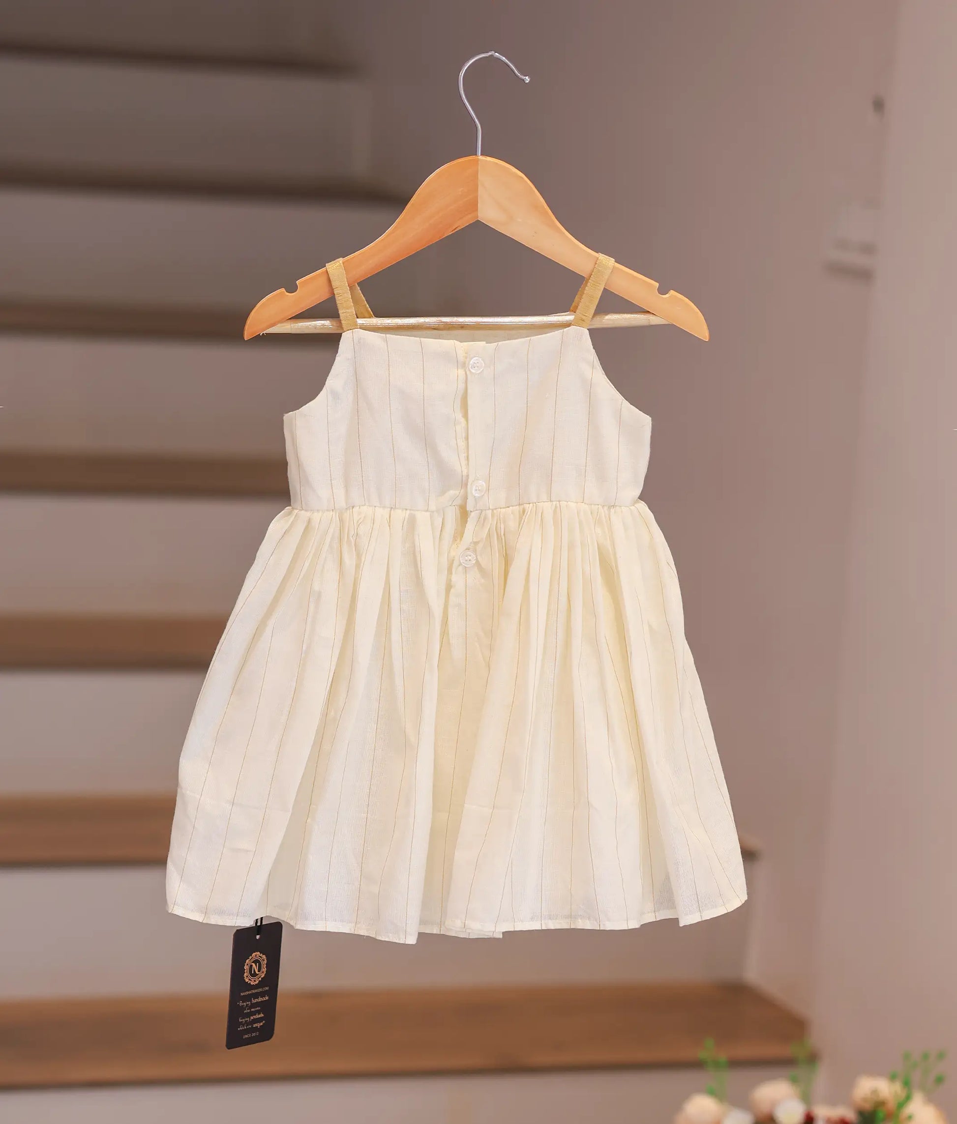 Back view of the off-white kasavu frock showing the gold straps and shirt button closure.