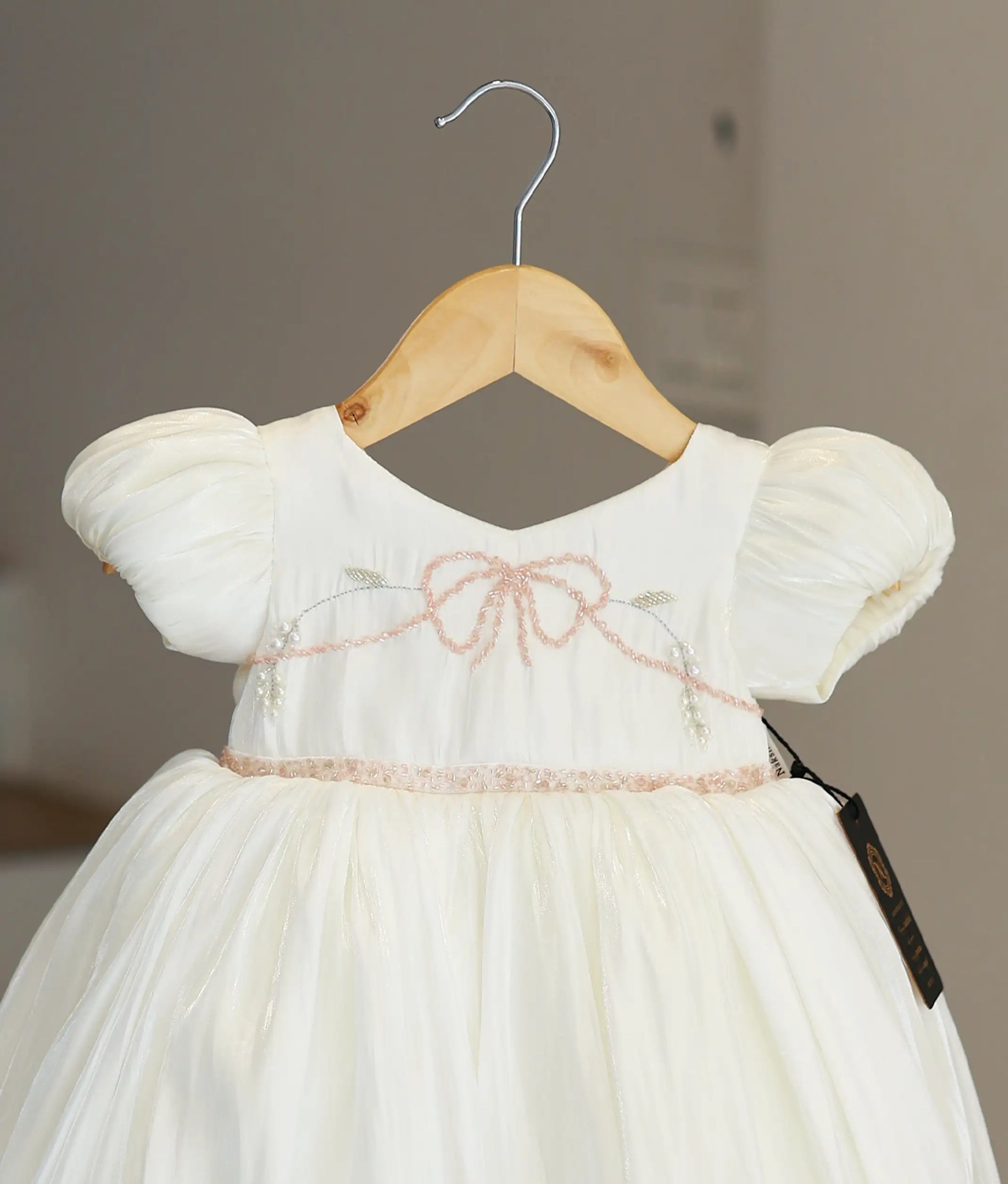 Close-up of the off-white frock highlighting the delicate handworked pink bead bow and floral embroidery on the chest.