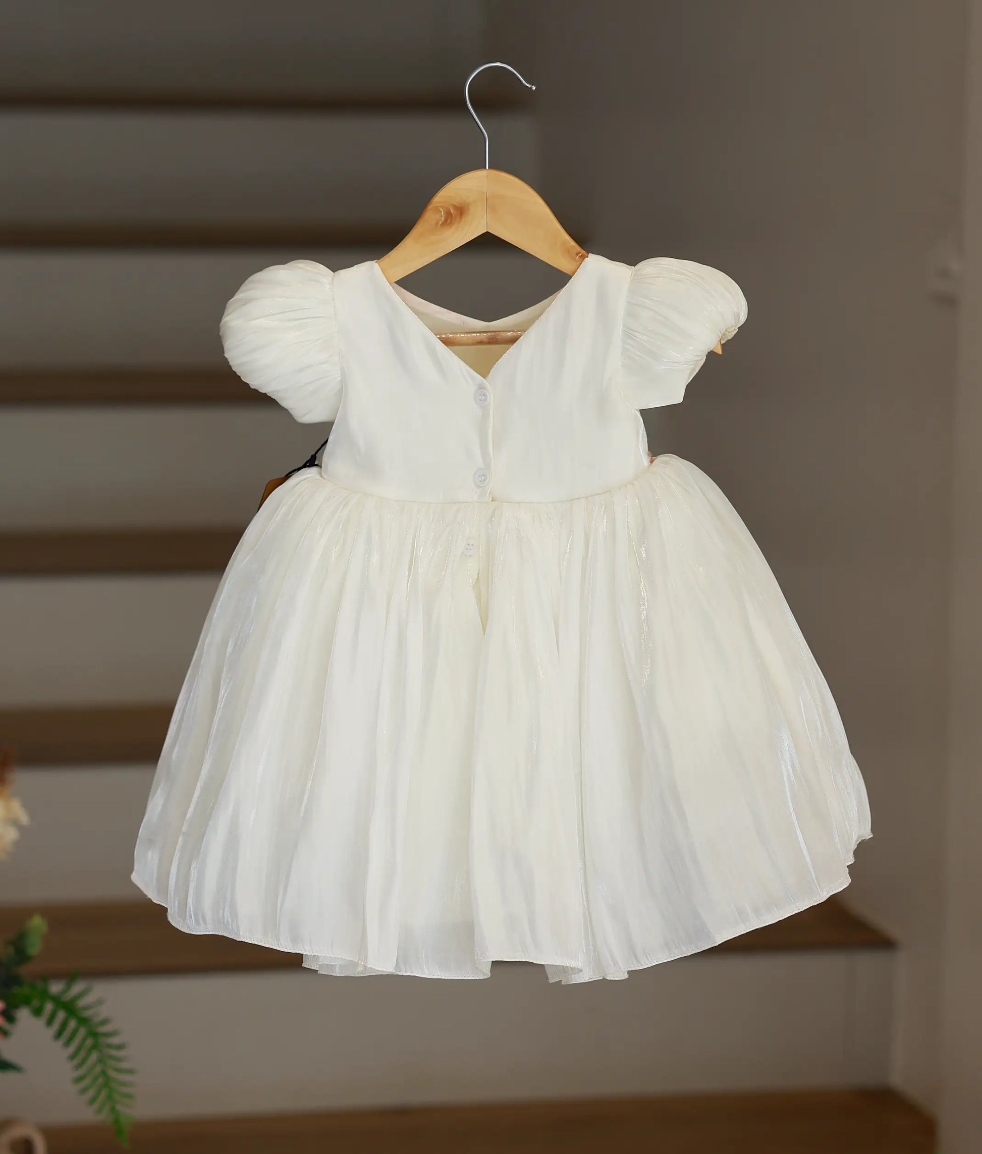 Back view of the off-white laser organza frock showing the elegant puffed sleeve profile and button closure.