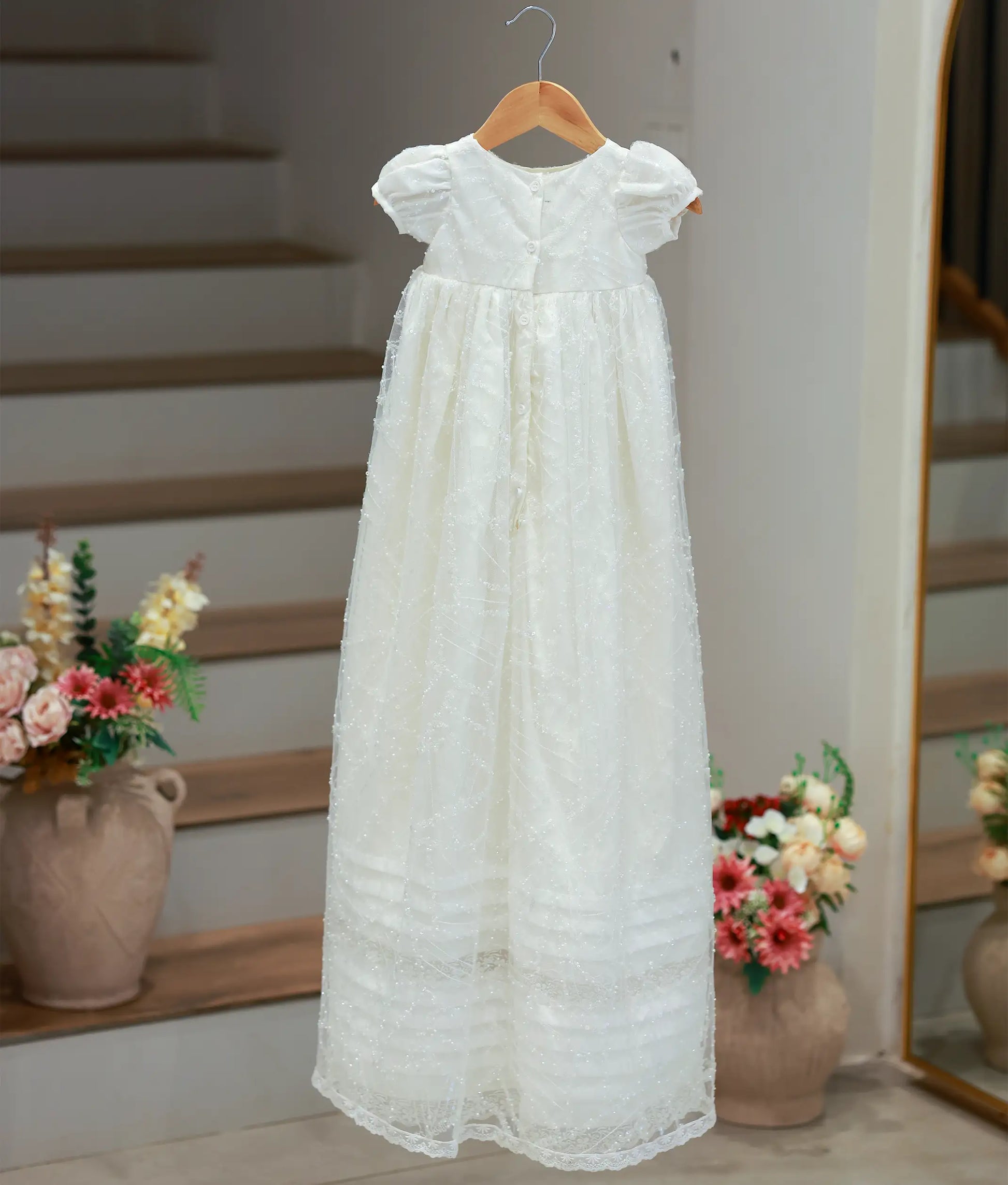 Back view of the long off-white baptism gown highlighting the functional button closures and the flowing pleated hemline