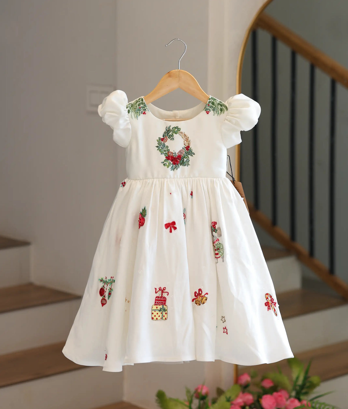 Front view of an off-white satin Christmas-themed dress featuring puff sleeves and festive hand embroidery on the flared bottom.