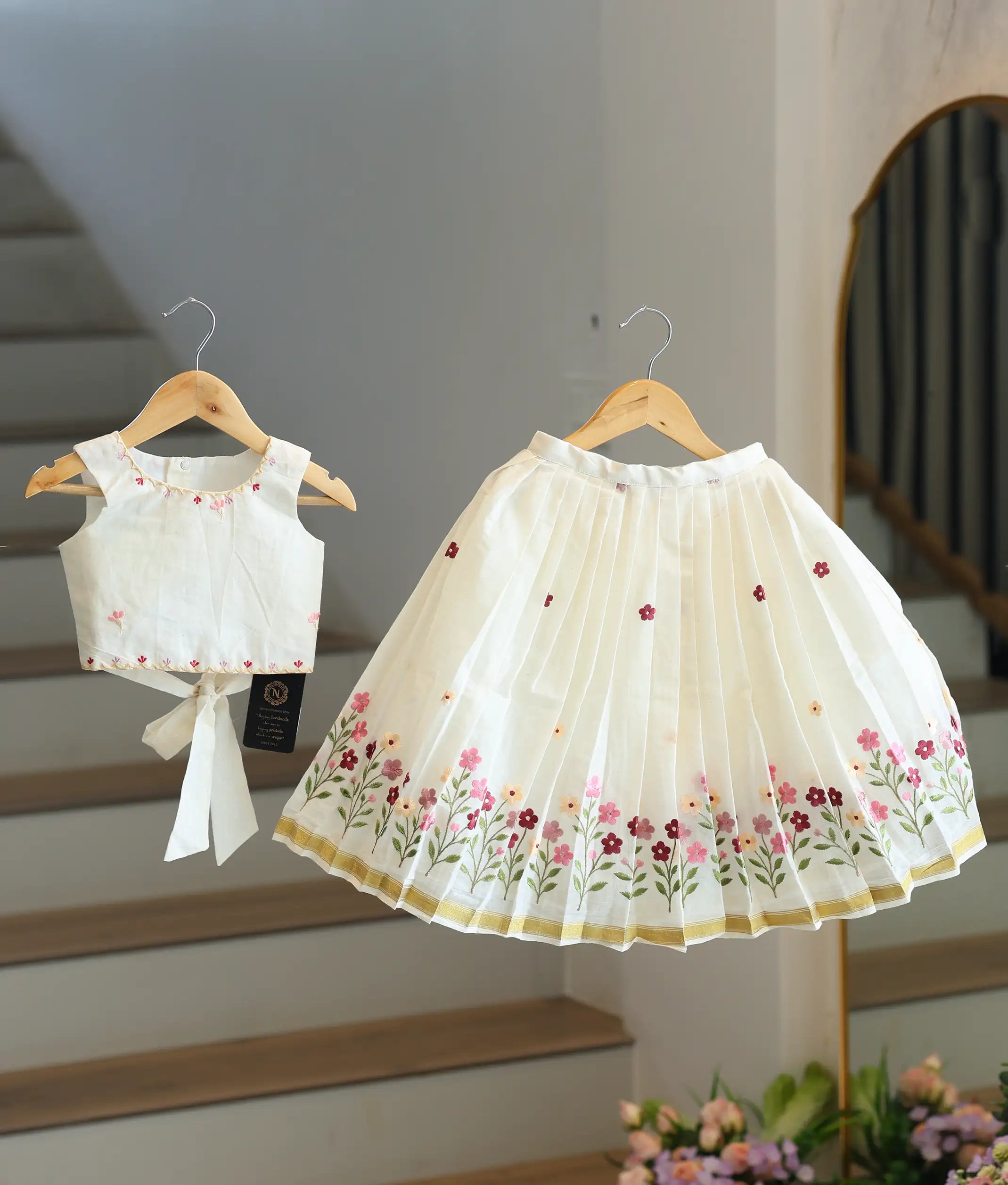 Front view of a girls' off-white skirt and top set with pink floral embroidery and a gold-bordered skirt.
