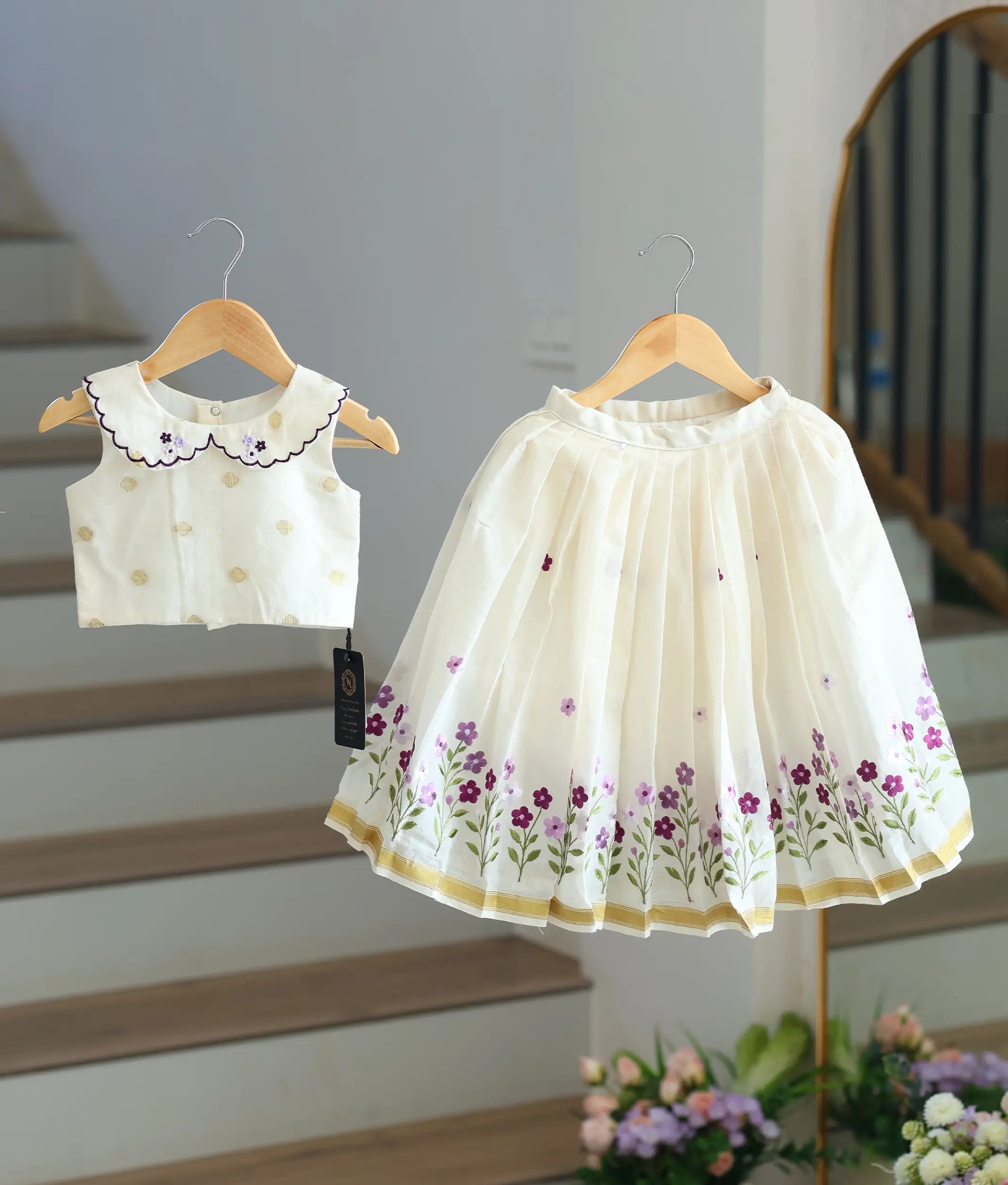 Front view of a girls' off-white skirt and top set with lavender floral embroidery and a gold-bordered skirt.