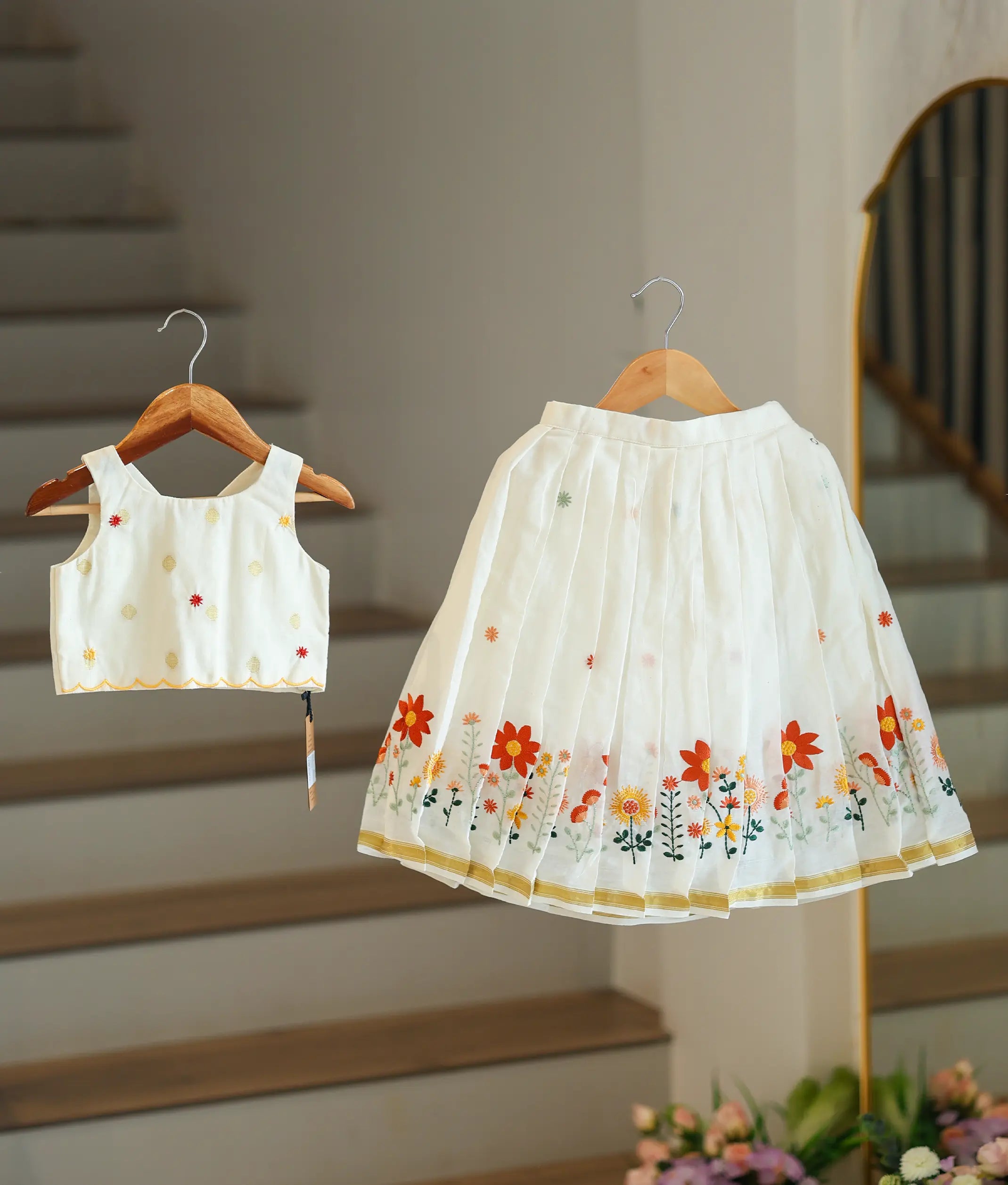 Front view of a girls' off-white skirt and top set with red floral embroidery and a gold-bordered skirt.